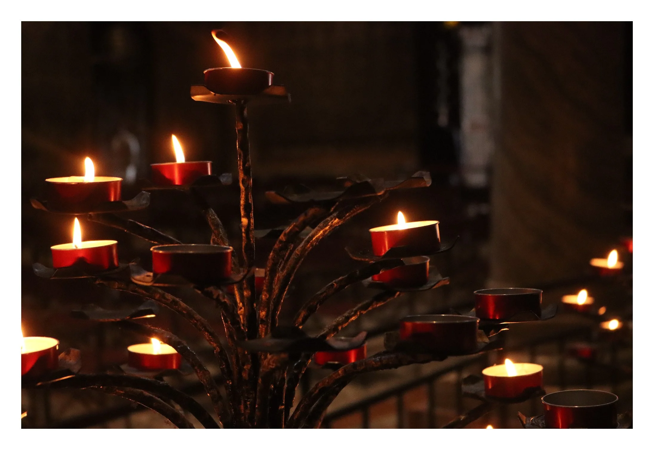 A metal candle holder with multiple small lit candles at night, casting a warm glow.