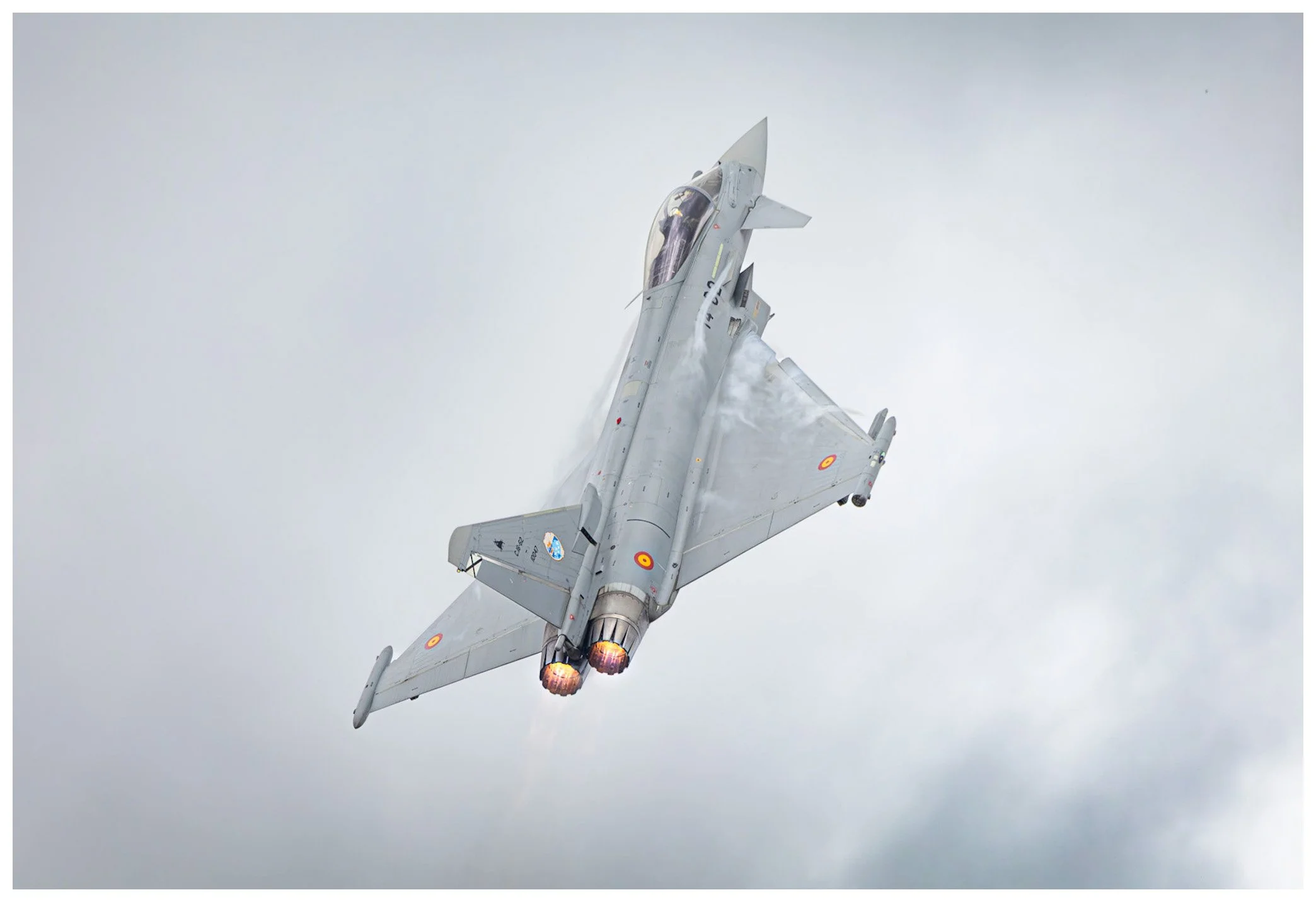 A fighter jet flying through cloudy sky with afterburners engaged.