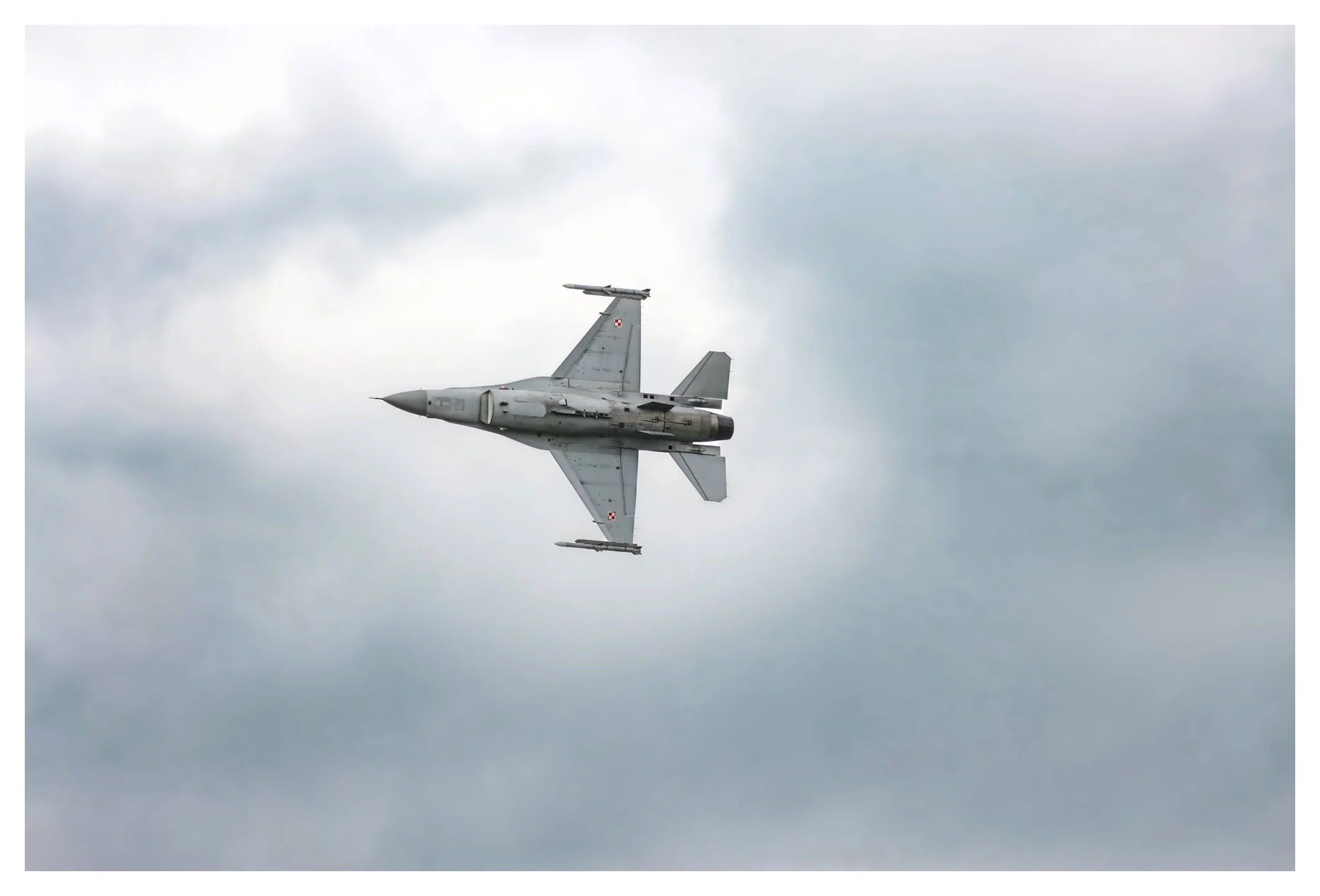 A gray military jet flying through a cloudy sky.