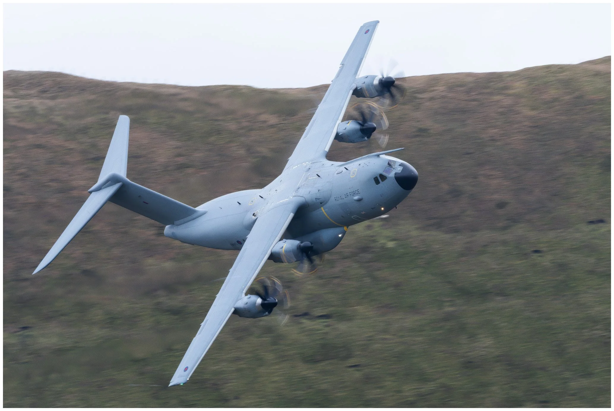 A military propeller aircraft flying at an angle over a landscape of grassy hills.