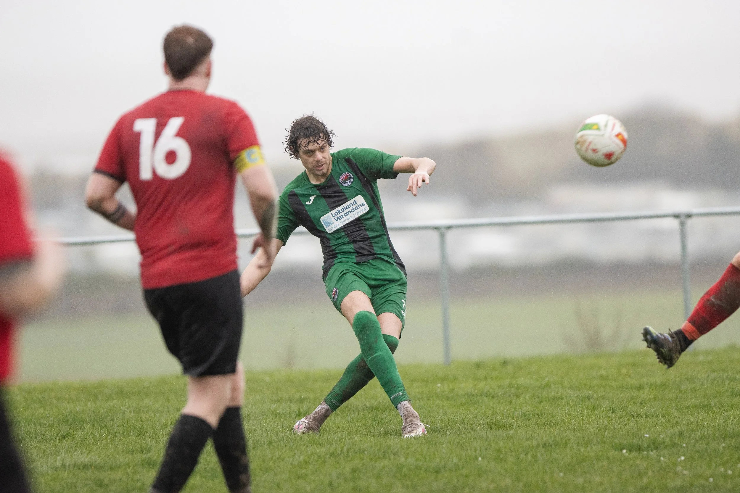 Soccer match with players in green and red uniforms outdoors on grass field