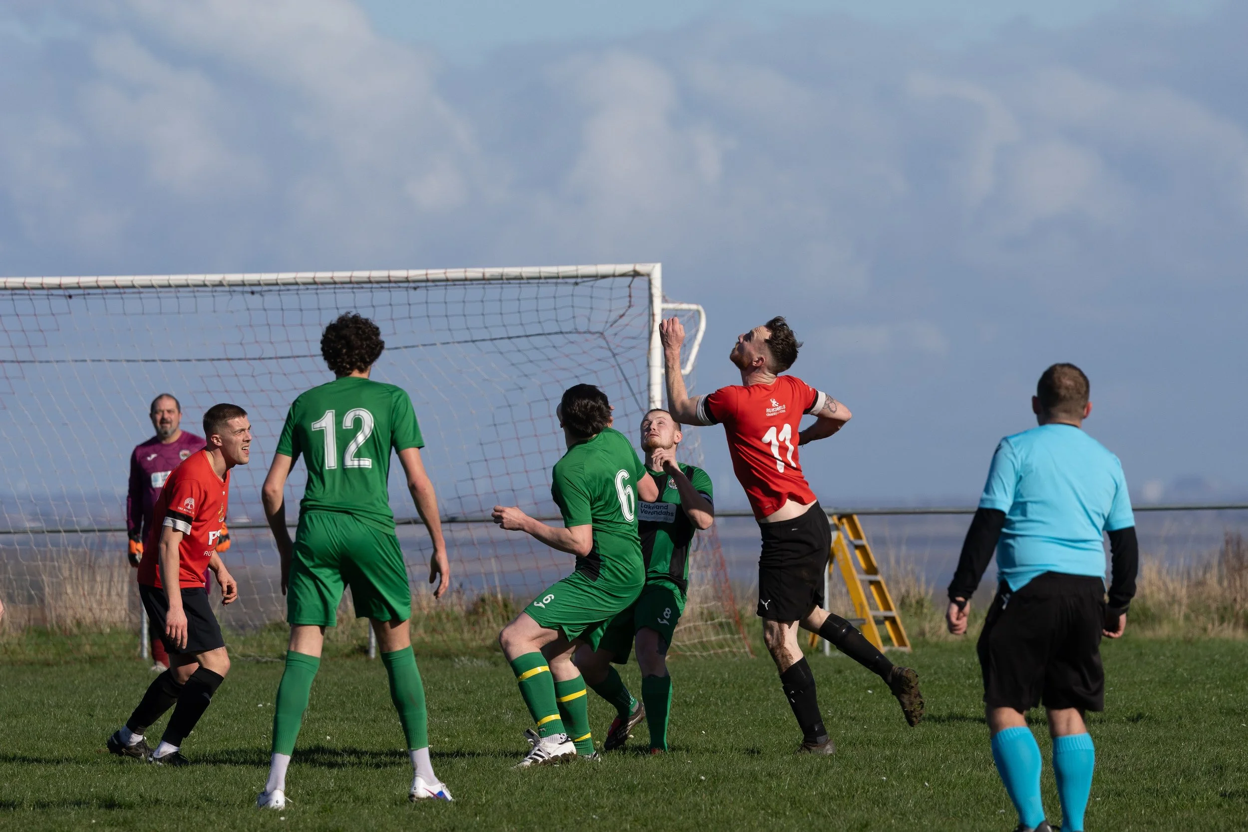 Soccer players and referee in action during a match on green field with goalpost and cloudy sky.