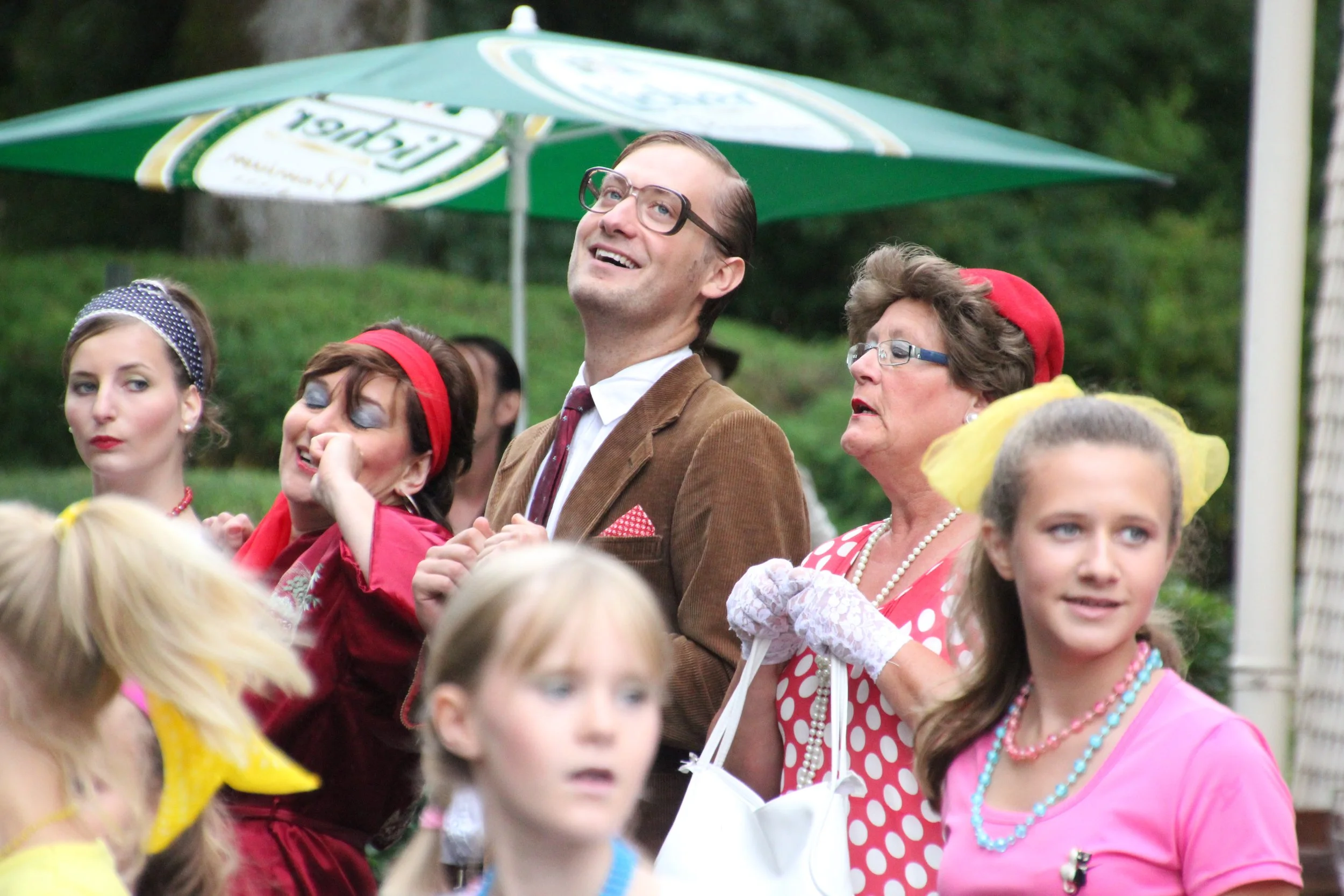 Menschen in bunten 50er Jahre Kostümen bei einer Party im Freien, unter einem grünen Sonnenschirm.