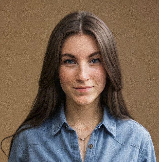 Porträt einer jungen Frau mit langen braunen Haaren, blauen Augen, trägt eine blaue Jeansjacke und einen kleinen Goldhalsreif.