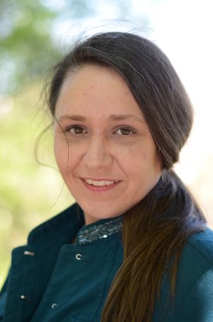 Bühnenbildnerin und Produktionsdesignerin Gesine Mahr Ein Porträt einer lachenden Frau mit dunklem Haar vor einem grünen, verschwommenen Hintergrund.