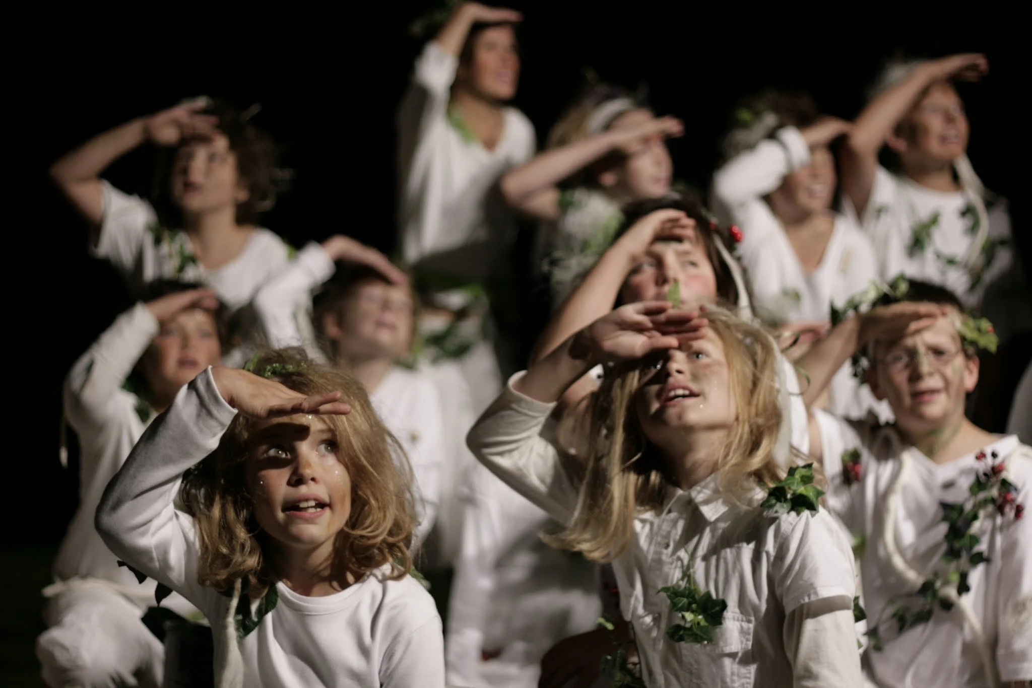 Kinder in weißen Uniformen mit Blattgirlanden auf dem Kopf, die einen Sonnenaufgang betrachten.