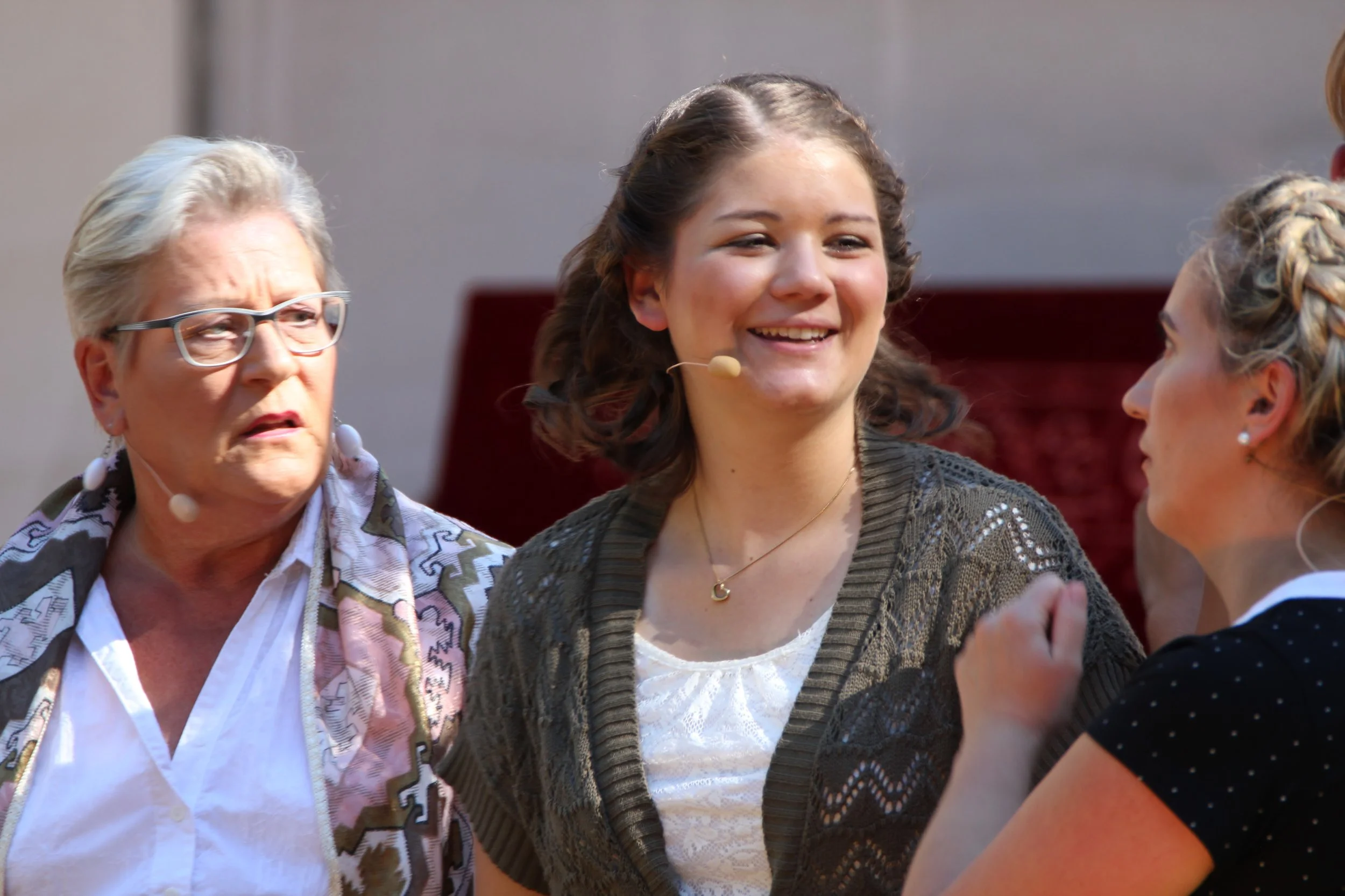 Drei Frauen im Gespräch, eine ältere Frau mit weißen Haaren, eine junge Frau mit dunklen, gewellten Haaren und eine junge Frau mit blondem Haar, alle tragen Mikrofone