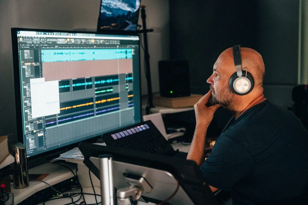 Ein Mann mit Kopfhörern arbeitet an einer digitalen Audio-Workstation auf einem großen Bildschirm, der Musik- und Audioaufnahmen zeigt.