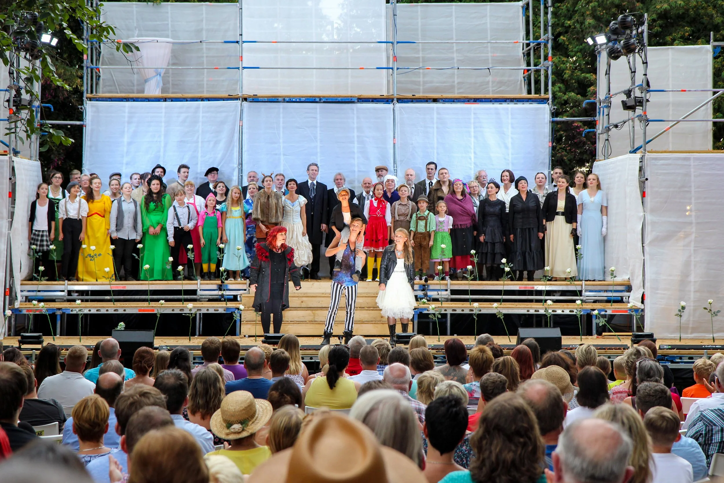 Eine Gruppe von Schauspielern auf einer Bühne bei einer Aufführung vor einem Publikum. Die Schauspieler tragen bunte Kostüme und sind in einer Reihe auf der Bühne positioniert. Das Ensemble der Birsteiner Festspiele 2016 und 2017 in: Der Wilde Grimm
