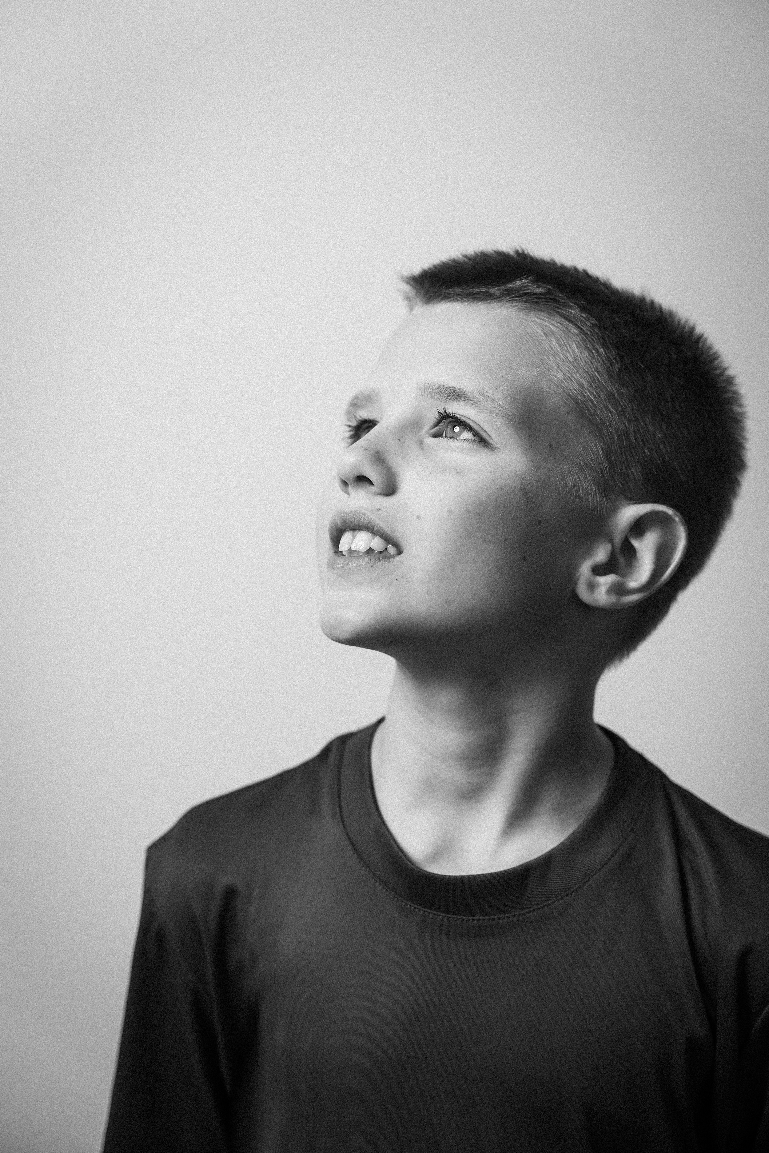 Junge mit kurzen dunklen Haaren und dunklem T-Shirt, blickt nach oben, auf einem grauen Hintergrund.