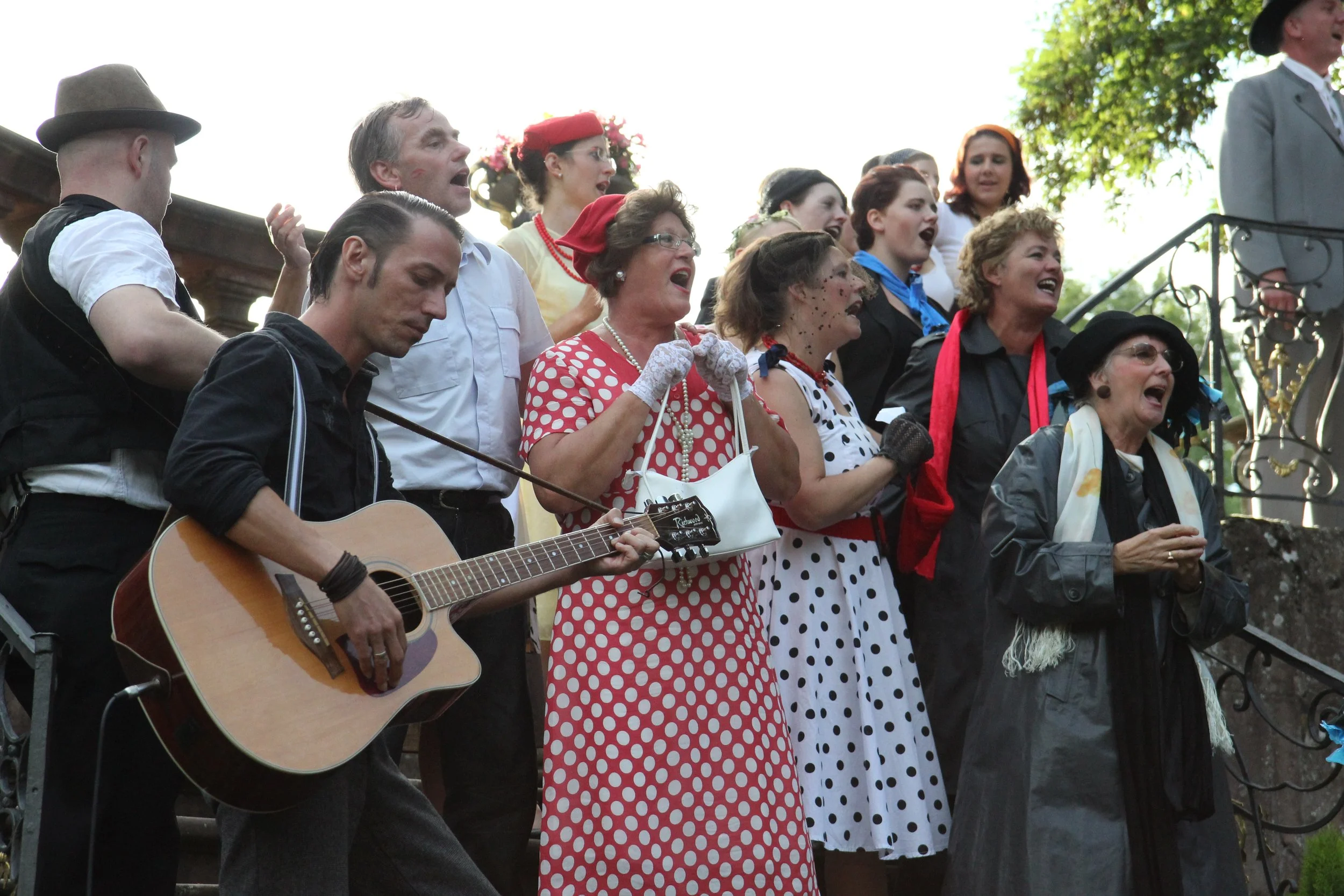 Menschen in vintage Kleidung singen und spielen Gitarre auf den Stufen draußen bei Sonnenschein.