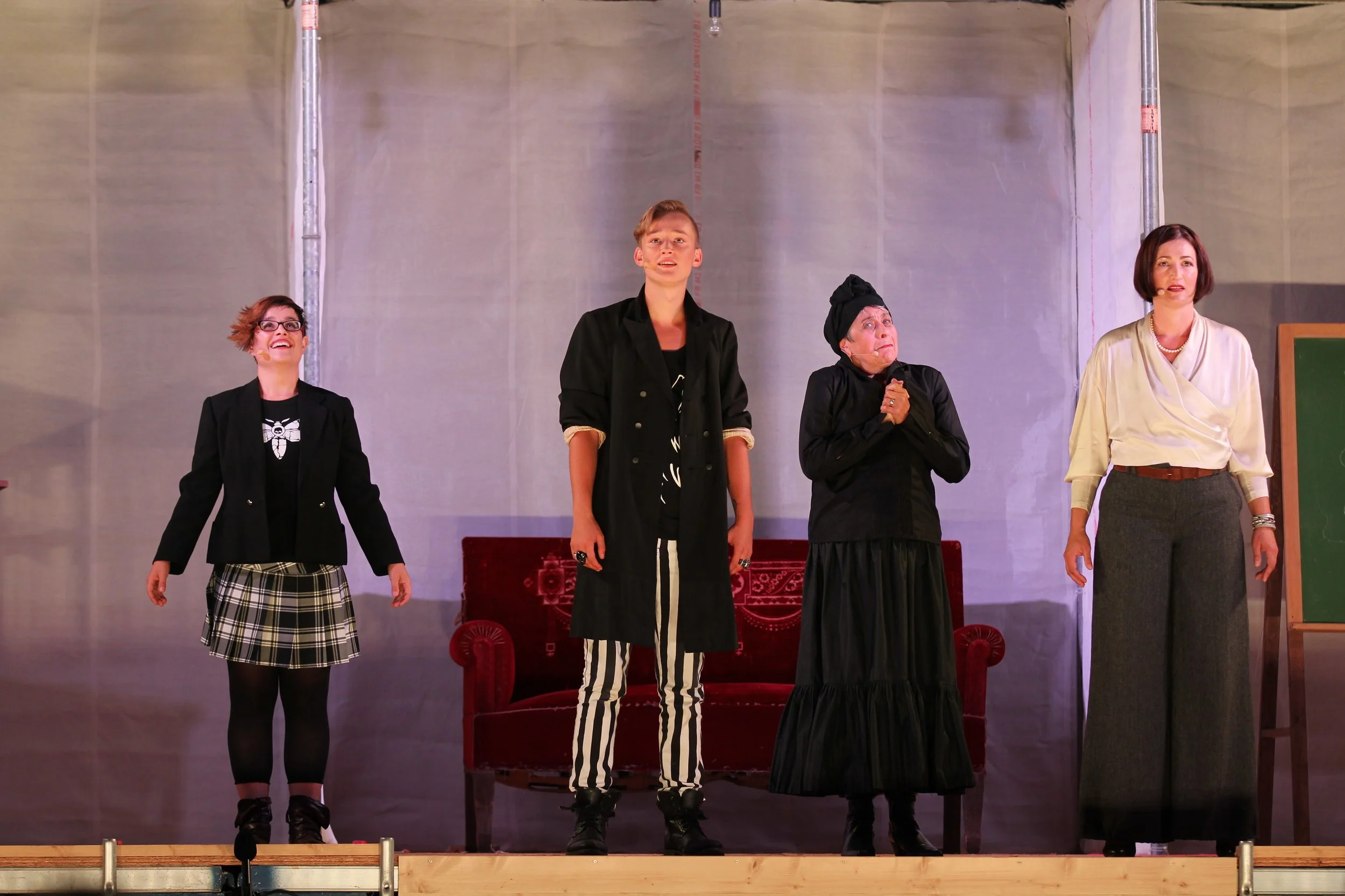 Vier Damen auf einer Bühne, die anscheinend in einer Theateraufführung auftreten, wobei die Frau in der Mitte sehr zu sein scheint.