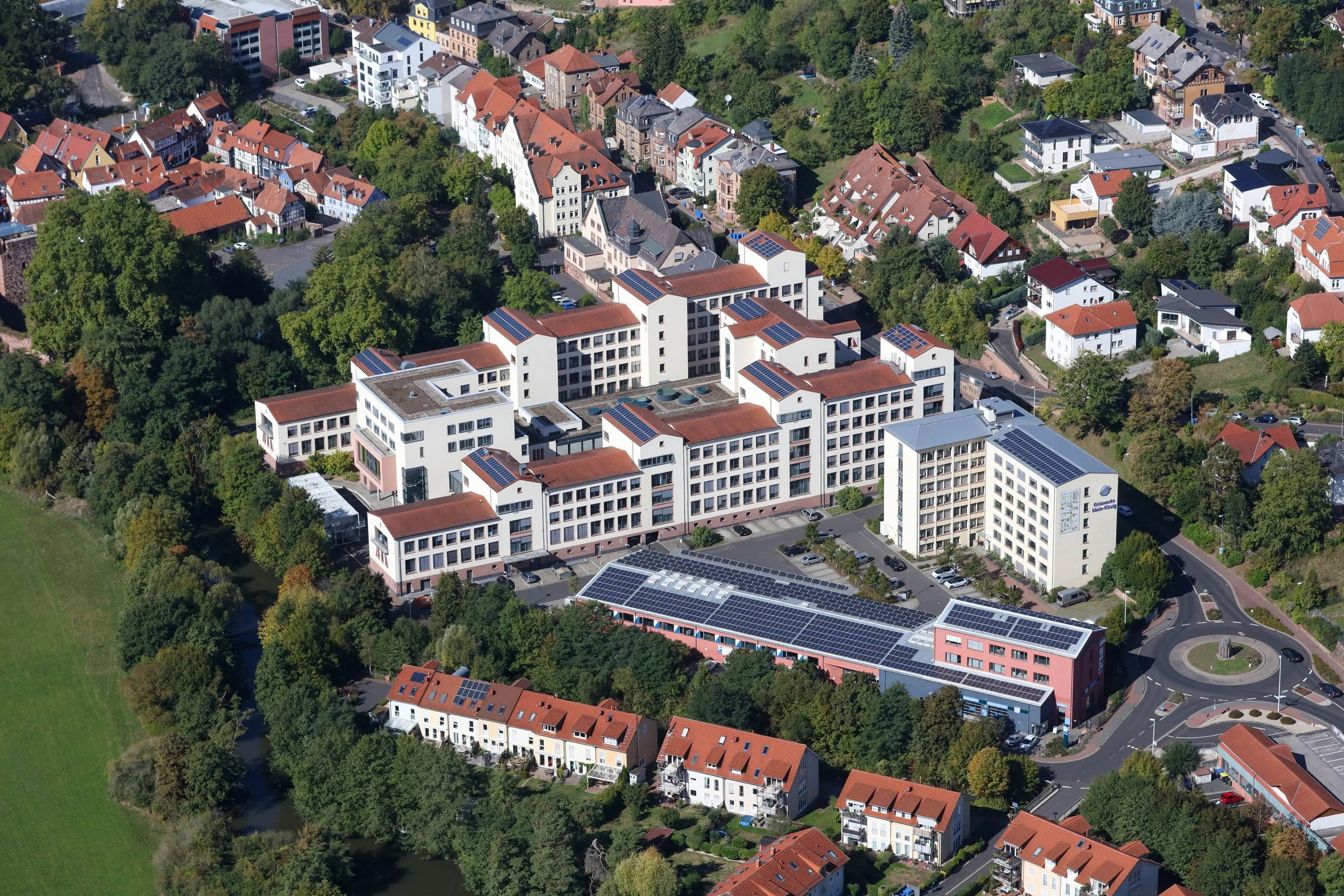 Luftaufnahme eines Stadtviertels mit einer Mischung aus modernen und traditionellen Gebäuden, umgeben von viel Grün und Bäumen.