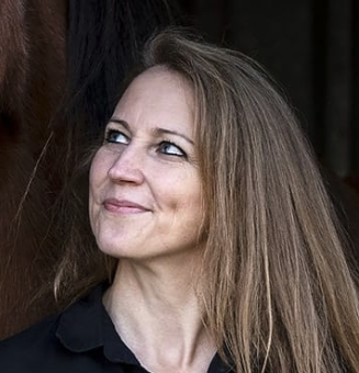 Eine Frau mit langem, blondem Haar, die nach rechts schaut, vor dunklem Hintergrund.