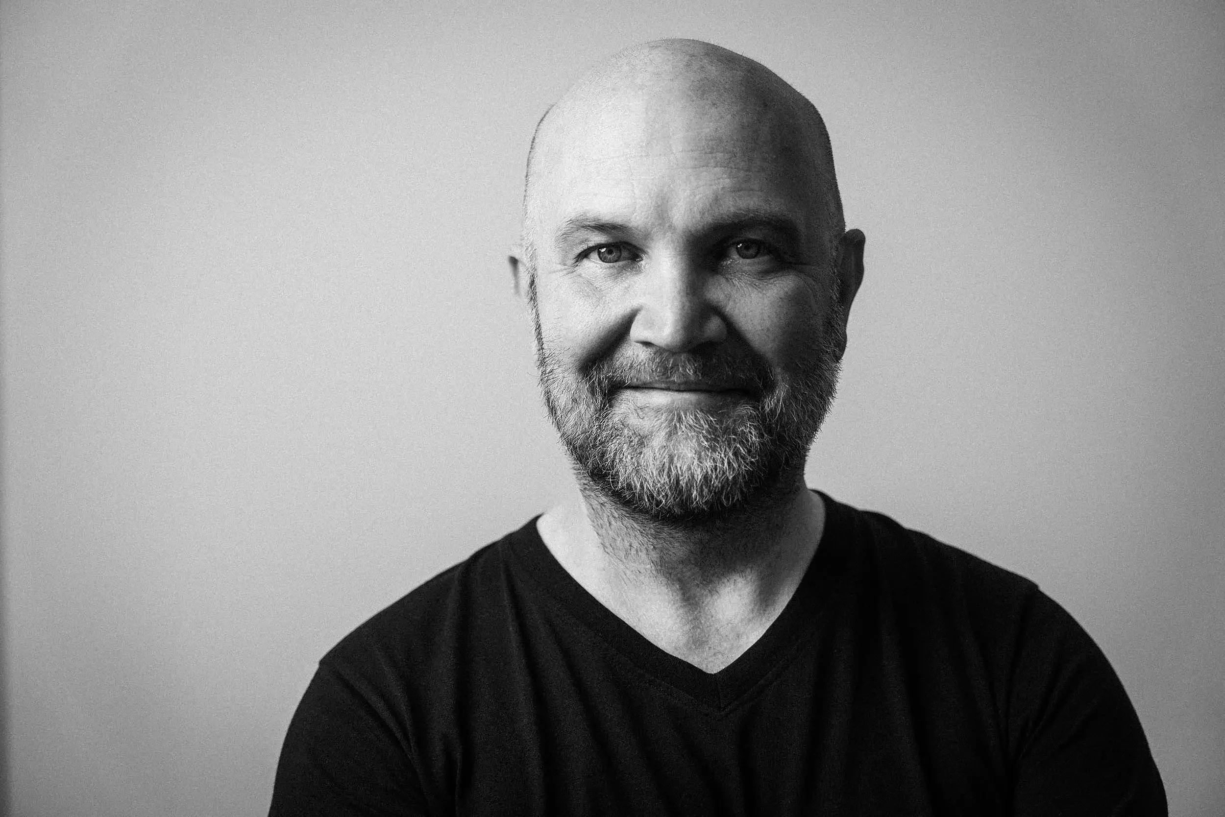 Schwarz-weiß-Fotografie eines lächelnden, barttragenden Mannes mit Glatze, trägt ein dunkles Shirt, vor hellem Hintergrund. Komponist Jochen Flach in  Das Wilde Weib – Das Musical · Birsteiner Festspiele 2027