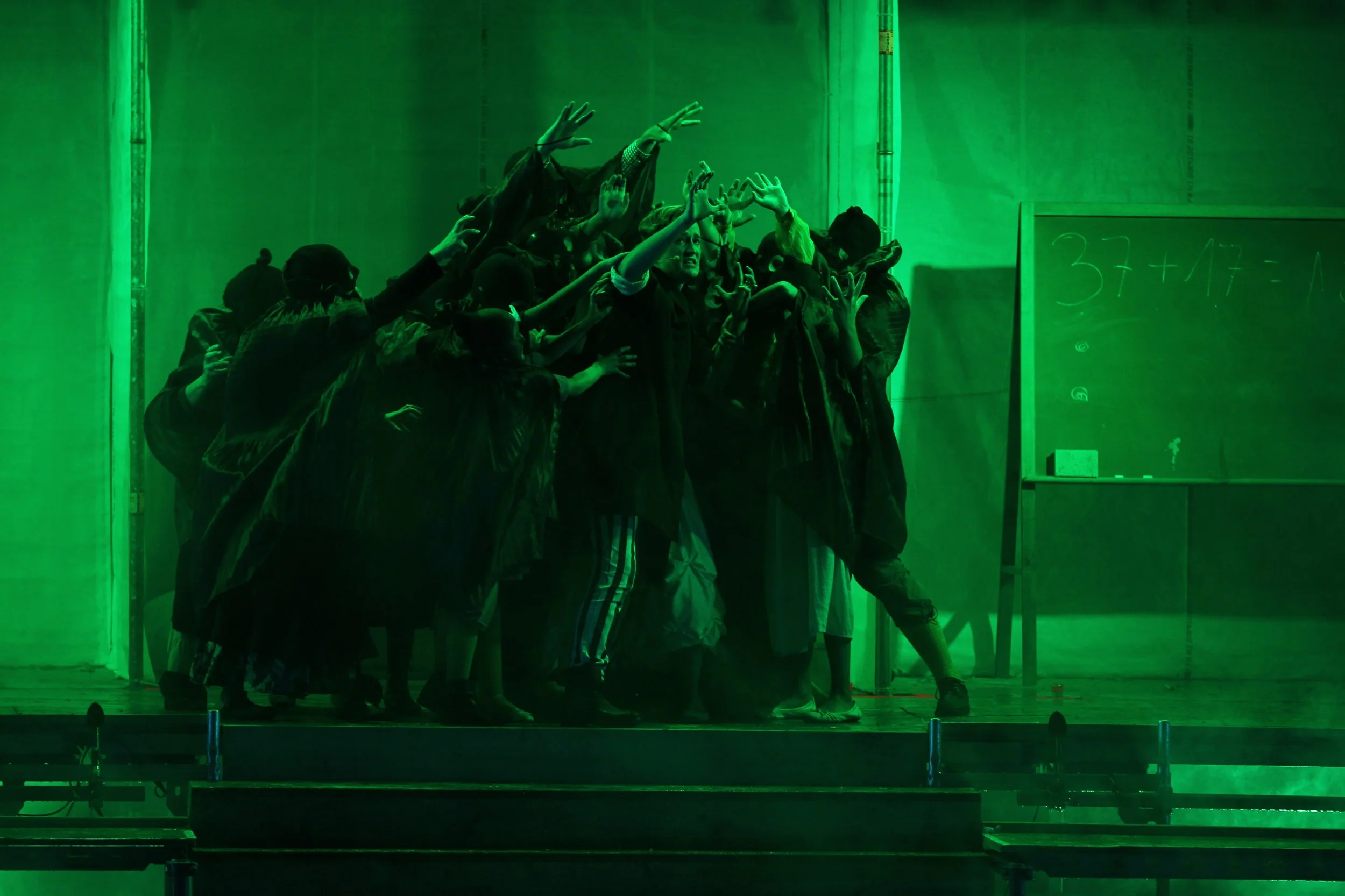 Schauspielgruppe in einem Theaterstück, umgeben von grüner Beleuchtung, vor einer Tafel mit einer mathematischen Gleichung. Das Ensemble der Birsteiner Festspiele 2016 und 2017 in: Der Wilde Grimm - Das Musical