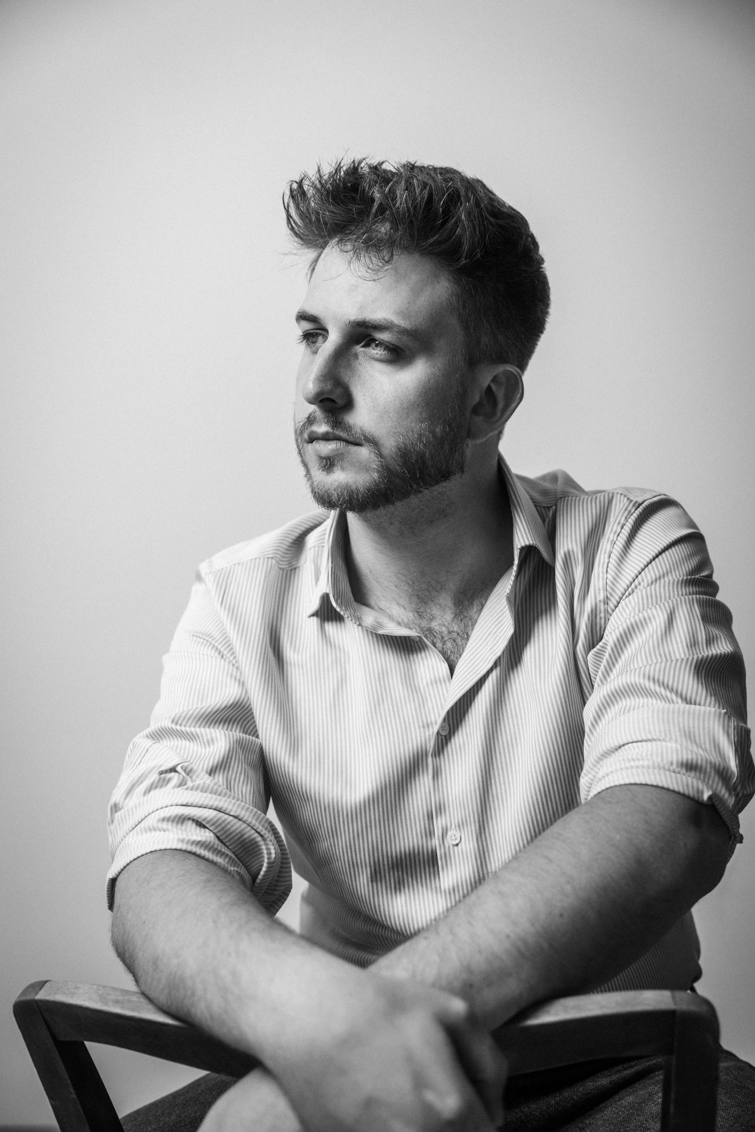 Schwarz-weiß-Foto eines jungen Mannes mit kurzen, lockigen Haaren und Bart, der nach rechts blickt, in einem Hemd mit offenem Kragen. Intendant Leon Roskoni  in  Das Wilde Weib – Das Musical · Birsteiner Festspiele 2027