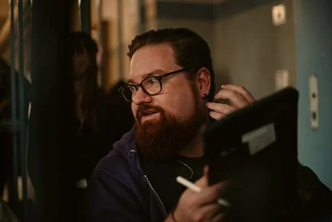 Autor der Birsteiner Festspiele 2020, Alexander Frank. Ein Mann mit Brille und Bart arbeitet an einem Computer in einer dunklen Umgebung.