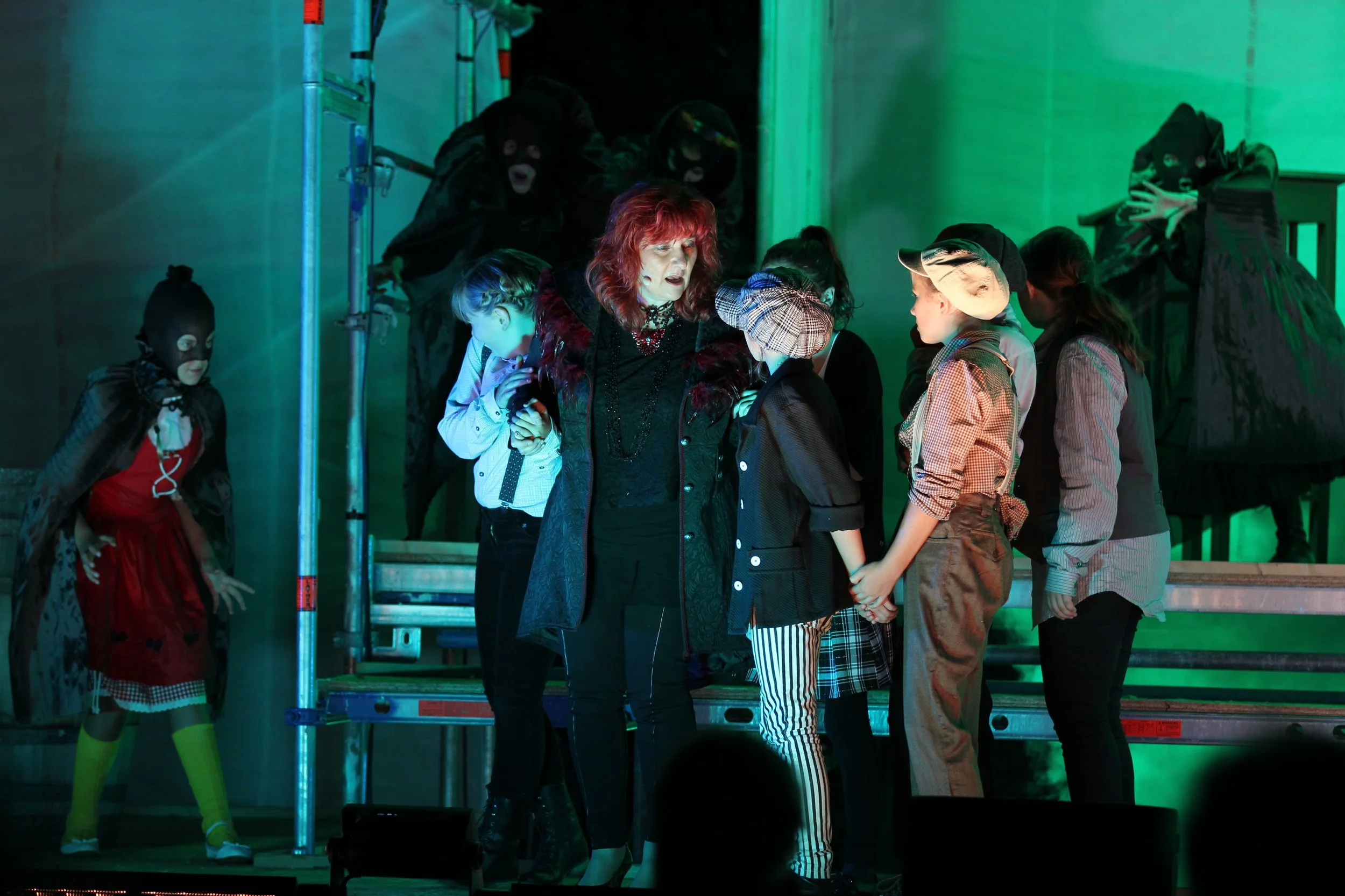 Eine Gruppe von Menschen, darunter Kinder und eine Frau, die auf einer Bühne bei einer Theateraufführung stehen, mit einigen Personen im Hintergrund in dunklen Kostümen. Das Ensemble der Birsteiner Festspiele 2016 und 2017 in: Der Wilde Grimm - Das M