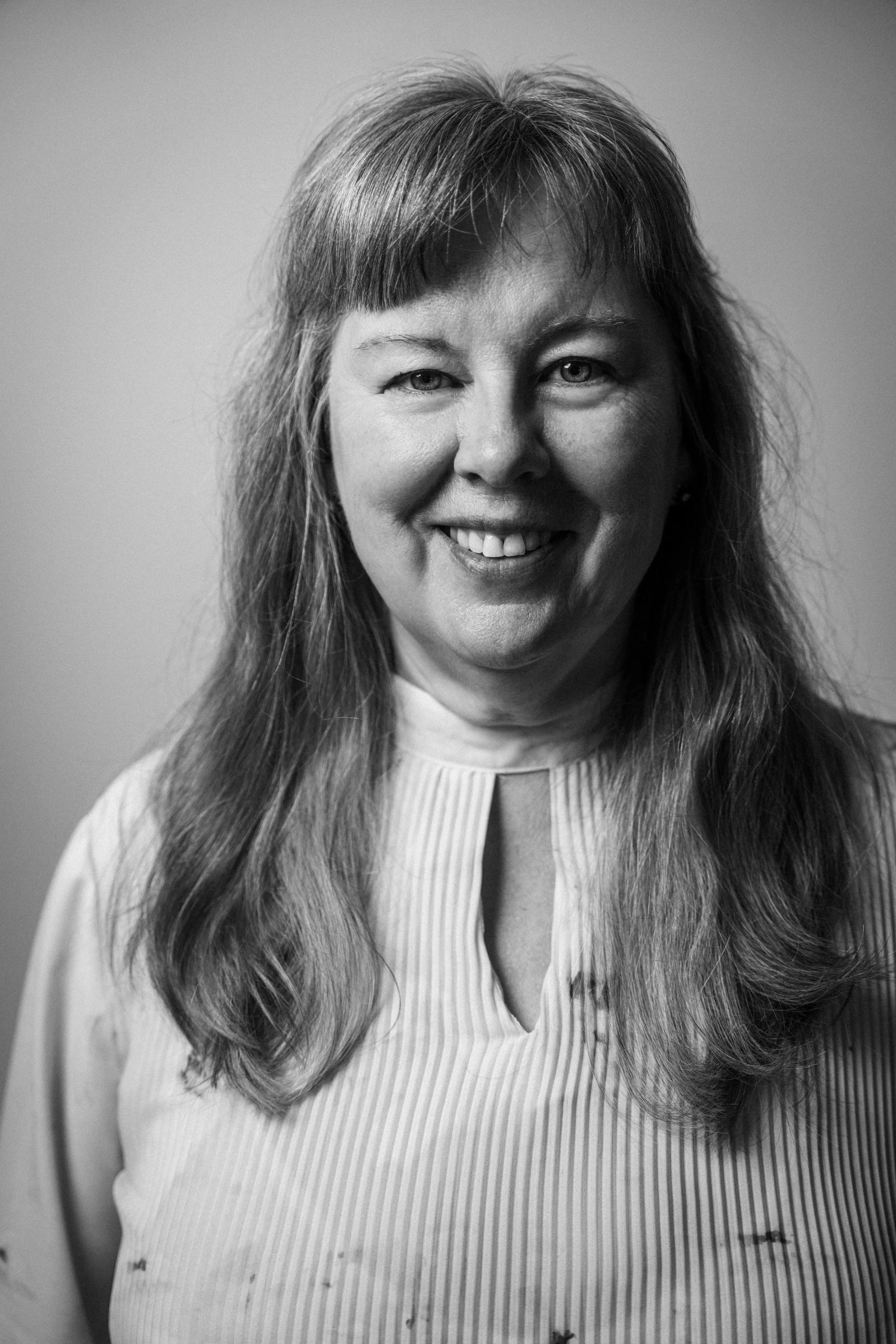 Schwarz-weiß Porträt einer lächelnden Frau mit langen, glatten Haaren, die eine gestreifte Bluse trägt. Beate Moritz-Mayer in  Das Wilde Weib – Das Musical · Birsteiner Festspiele 2027
