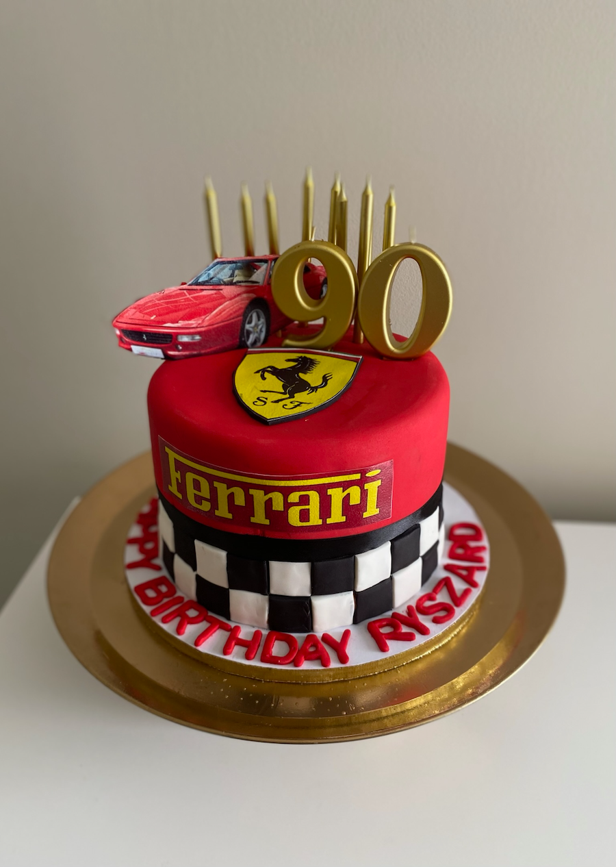 A Ferrari-themed birthday cake for Rye Szard, with a red car topper, Ferrari logo, black and white checkered pattern, and gold '90' candles.