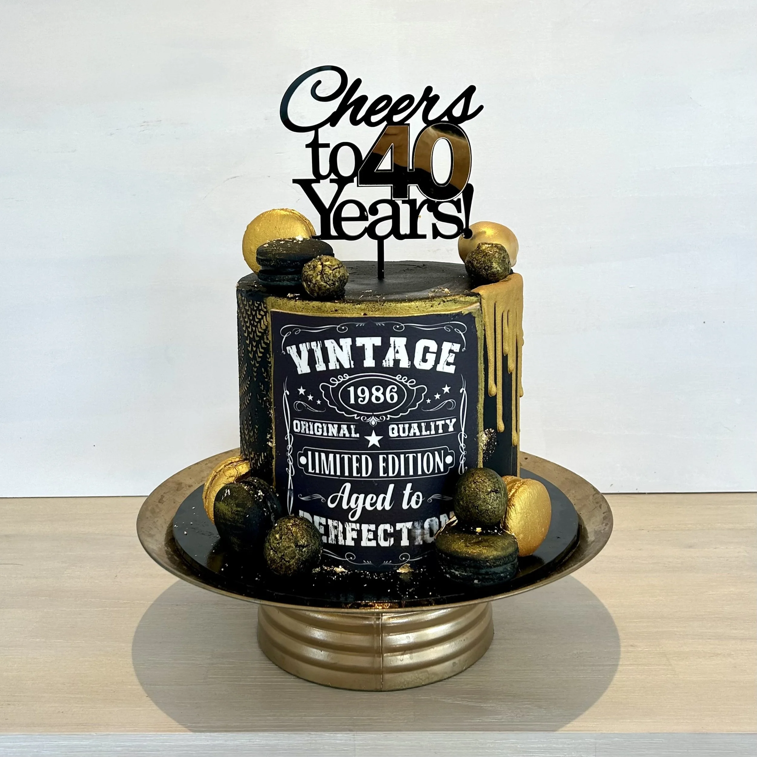 Gluten Free chocolate cake layers filled with chocolate ganache buttercream and covered in black buttercream, macarons, and handmade cake balls, edible icing image. 