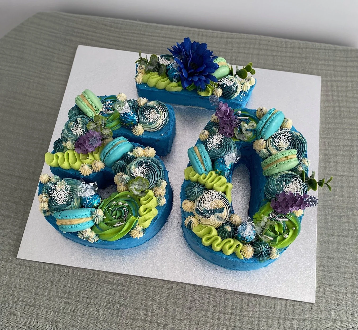 Red velvet cake layers filled with cream cheese filling, vanilla buttercream piped in bright green and blue, 50 number cake with crown.