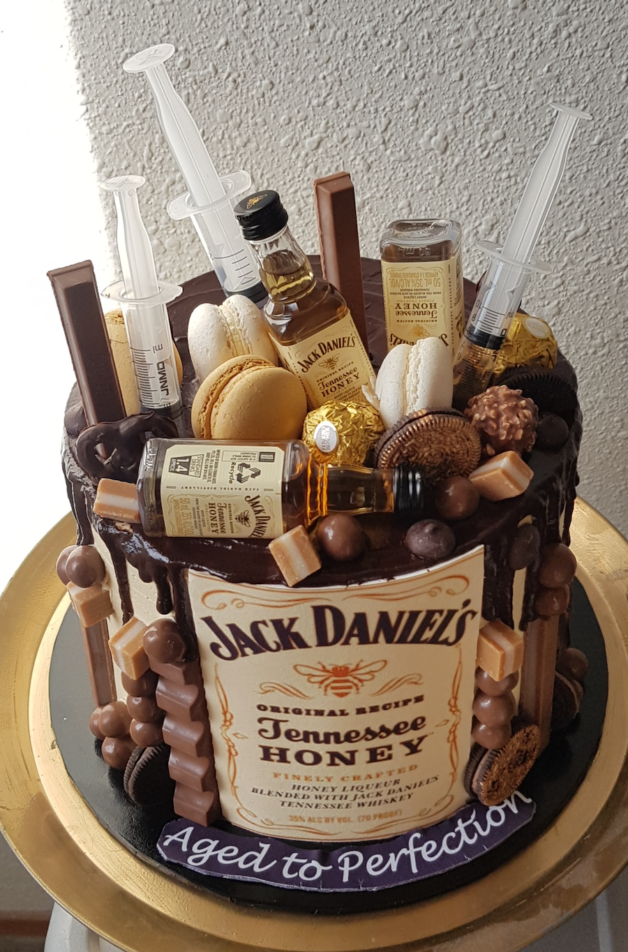 A luxury cake decorated with Jack Daniel's Tennessee Honey whiskey bottles and assorted candies and chocolates, resembling a whiskey bottle with whiskey-themed decorations on top.