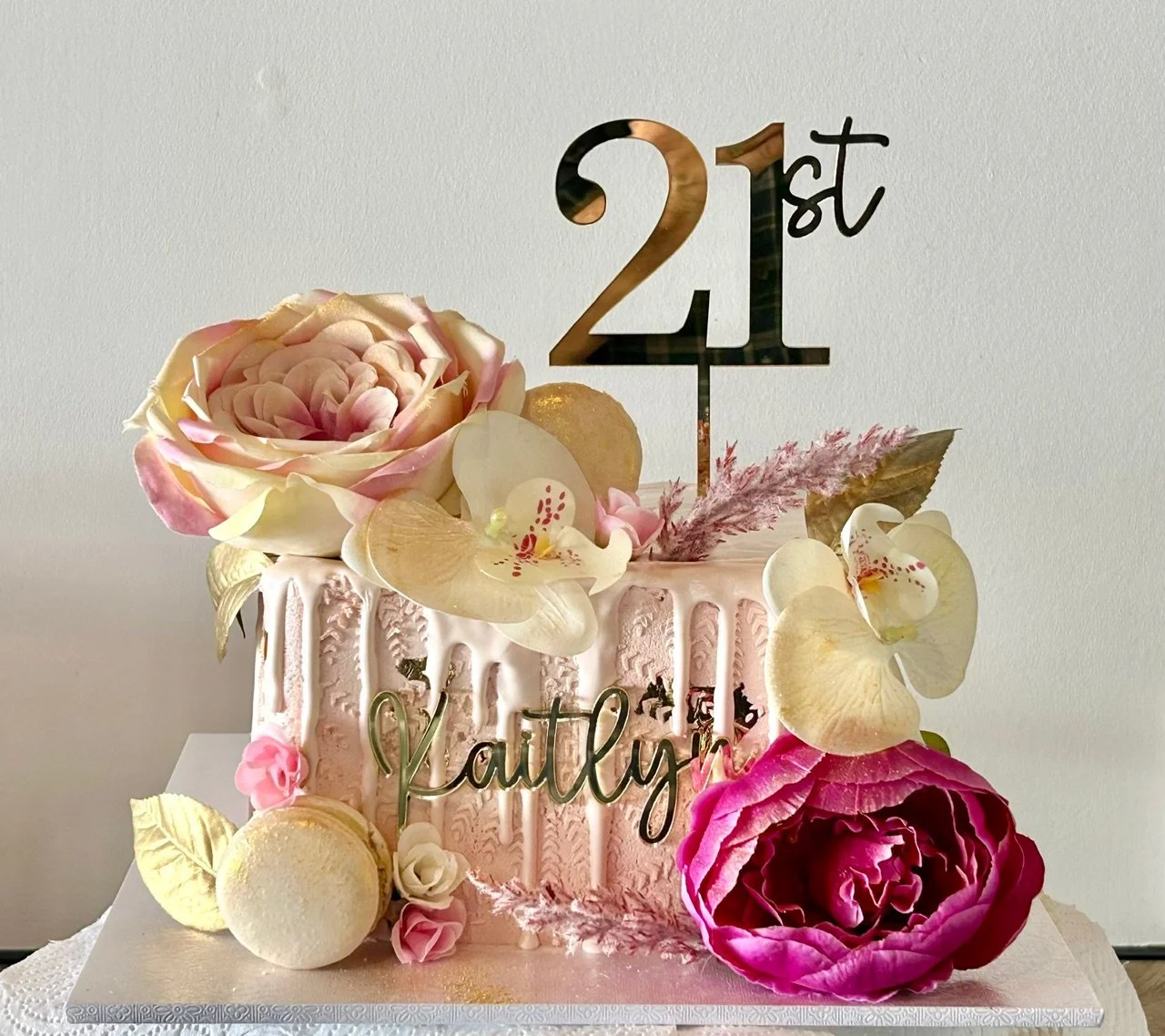 A square red velvet cake with cream cheese filling, vanilla buttercream with white chocolate ganache drip and stencilled detail, gold leaf, macarons and artificial flowers. 