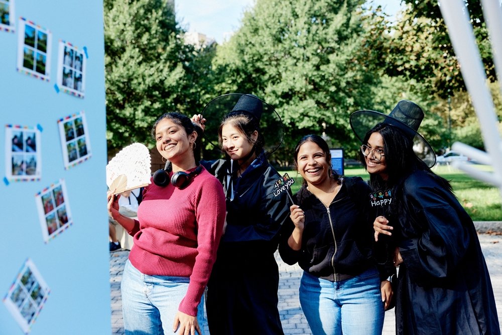 Students at an Ivy League university (Brown University) celebrating Korean culture at a 'Hangeul Truck' event, wearing traditional Korean Gat hats and holding signs that say 'I love you' and 'Happy' in Korean.