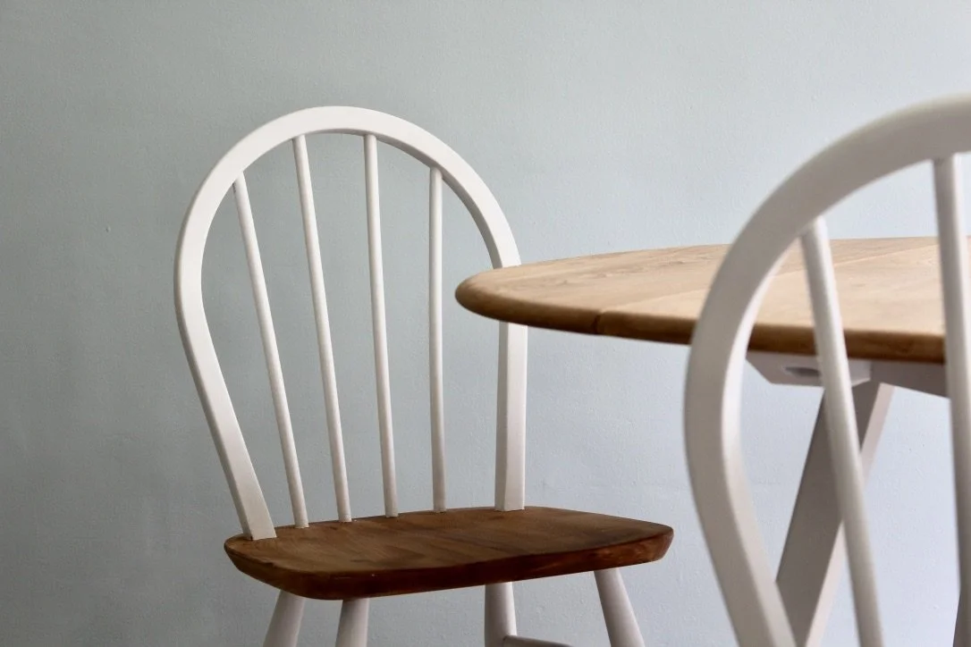 A wooden chair with a white frame next to a wooden table against a light gray wall.