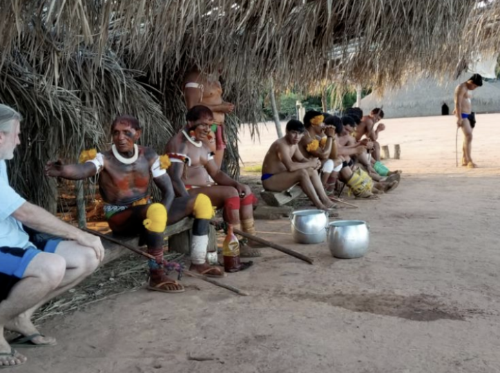 Group of children and adults outdoors raising their hands, smiling, with plants and trees in the background.