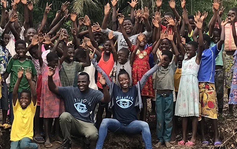 Group of children and two adults outdoors, smiling and raising their hands in celebration.