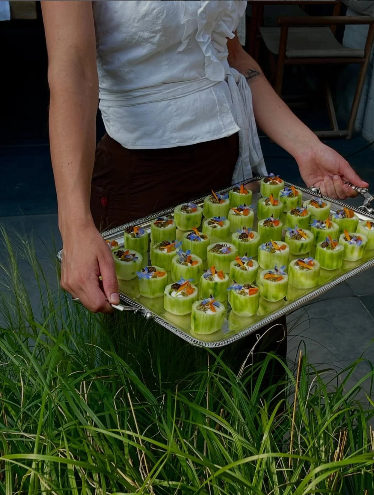 A tray of summer canapés carried outdoors through tall grass
