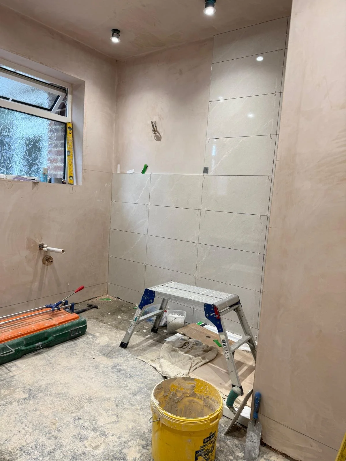 A bathroom under renovation with tiles partially installed on the wall