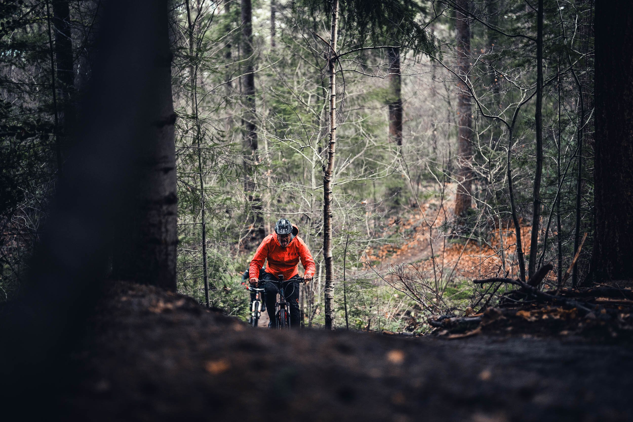 A person riding a mountain bike in a forest, wearing a helmet and red jacket.