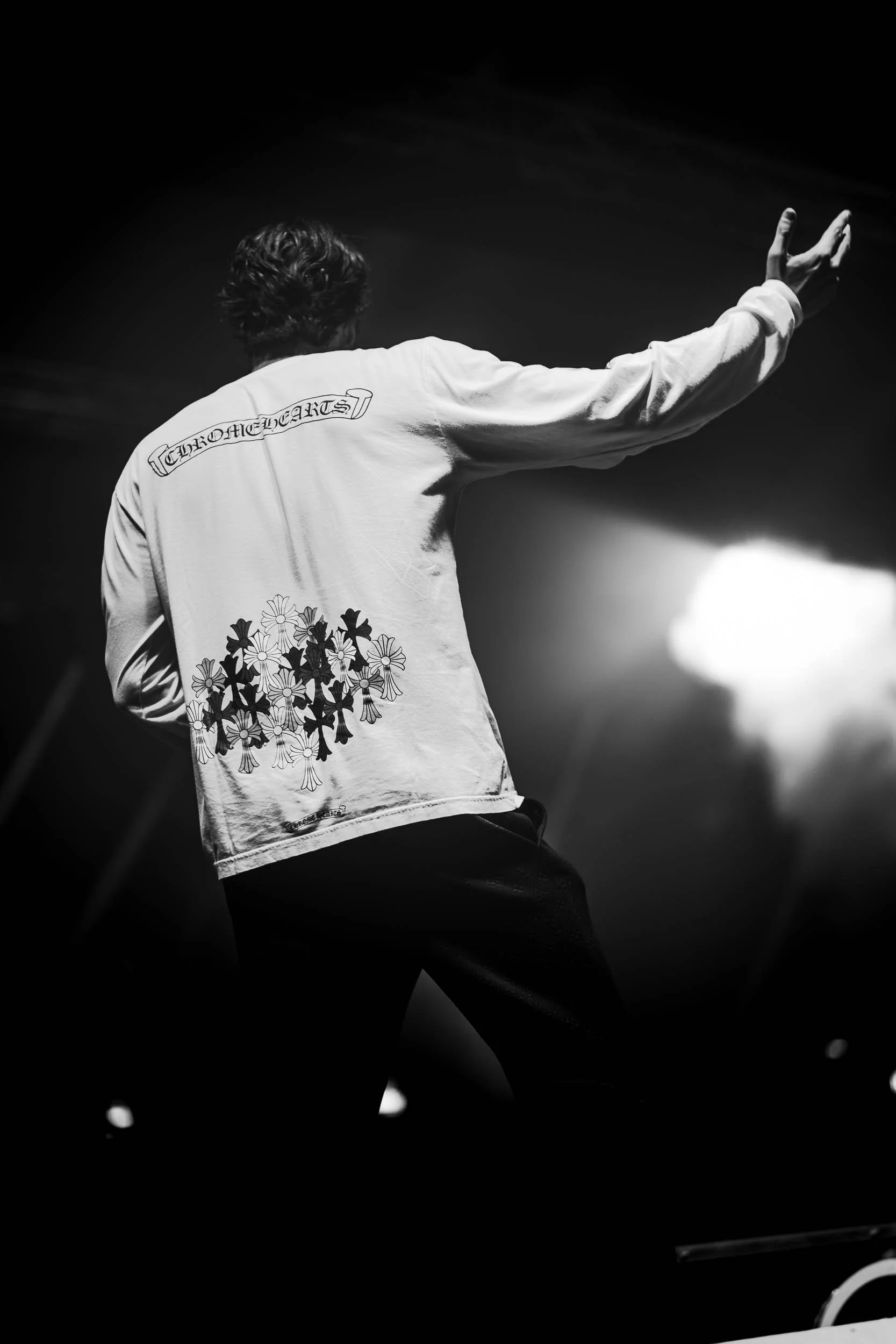 A man performing on stage, viewed from behind, wearing a long sleeve shirt with floral patterns and text on the back, in black and white.   (Viktor Verhulst)