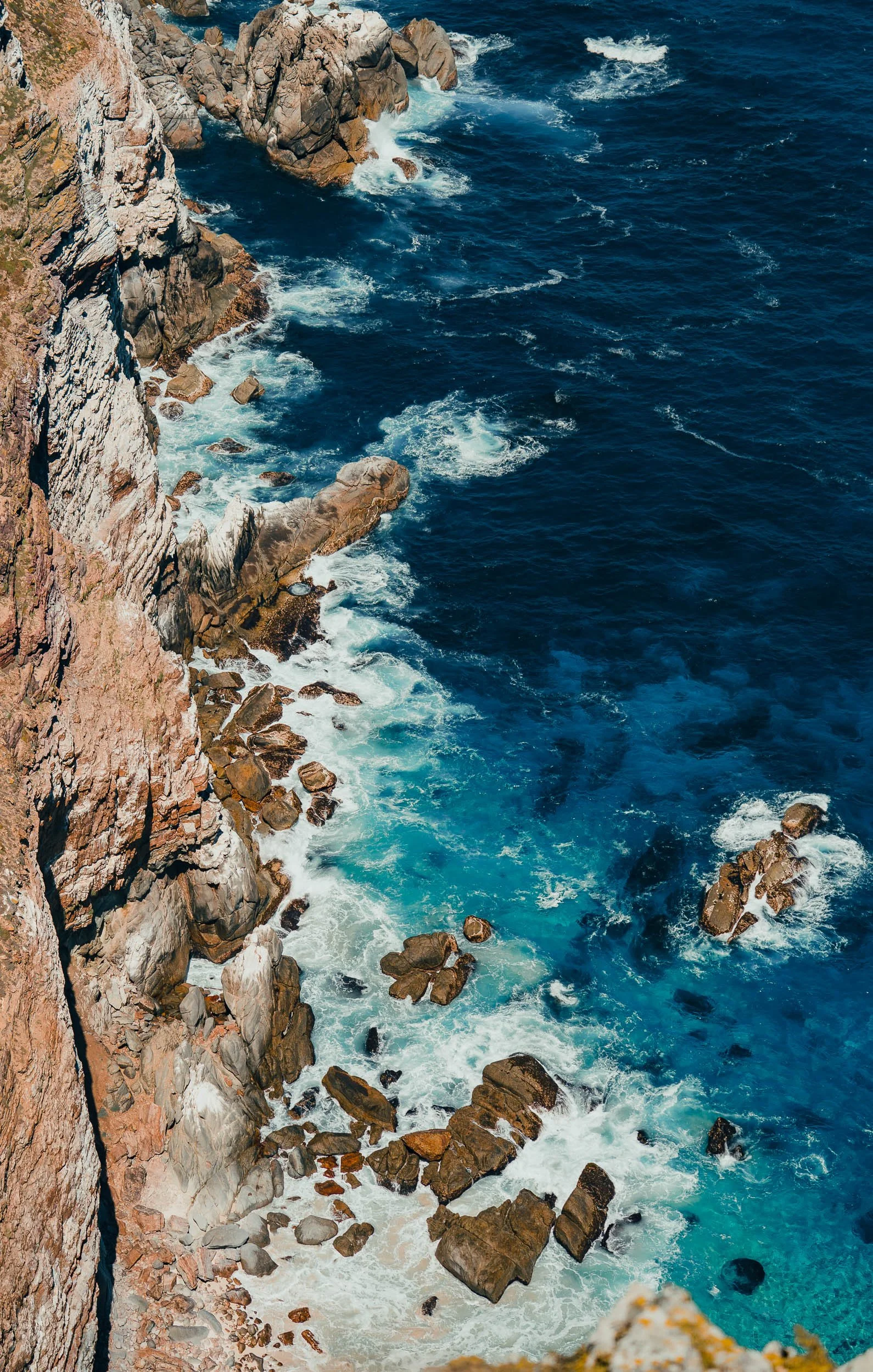 Cliffside view of water crashing against rocks along a rugged coastline.