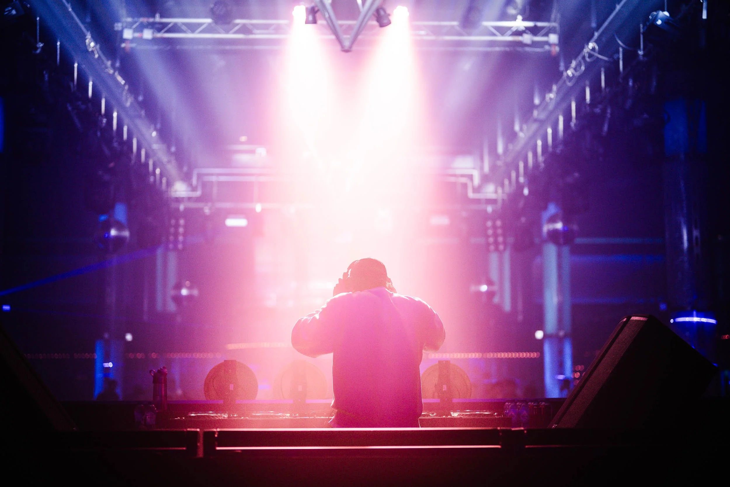 DJ performing at a concert with bright pink and purple lights illuminating the stage.   (Viktor Verhulst)