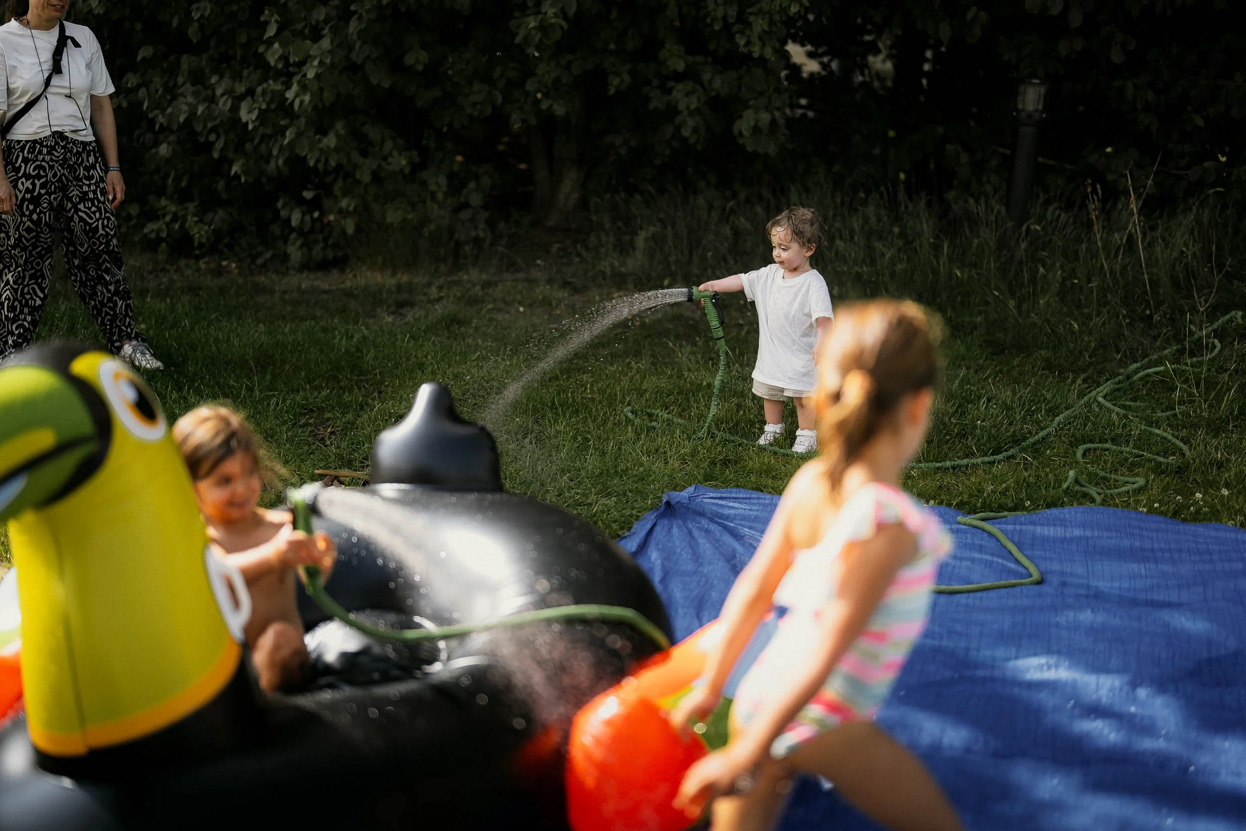 Children playing with water hose and inflatable float in a grassy yard during daytime. (Graveller)