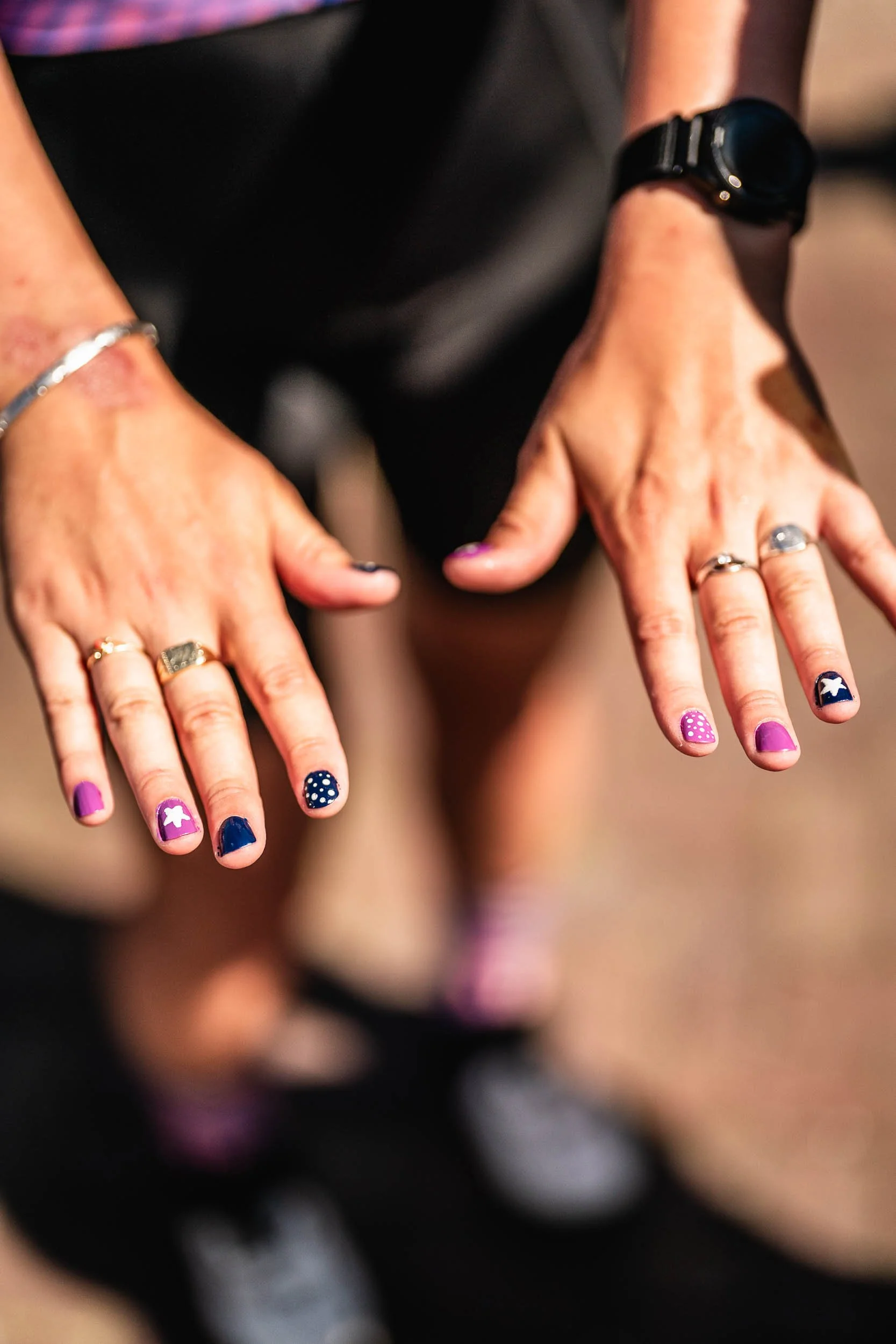 Close-up of a person's hands with colorful painted nails and rings, showing the palms facing downward. (Patta.nl Rapha)