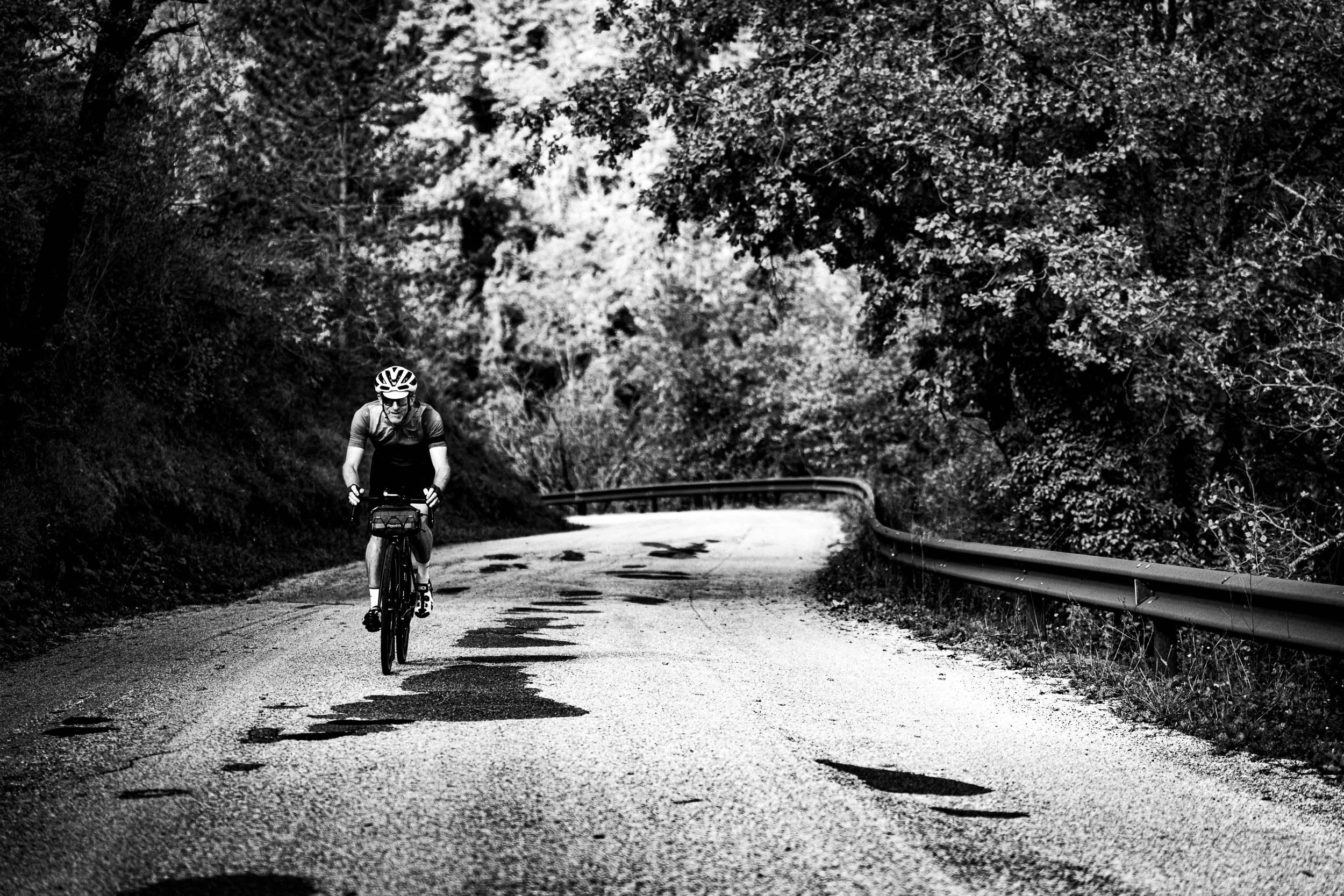 A person riding a bicycle on a winding, uneven road surrounded by dense trees and foliage.