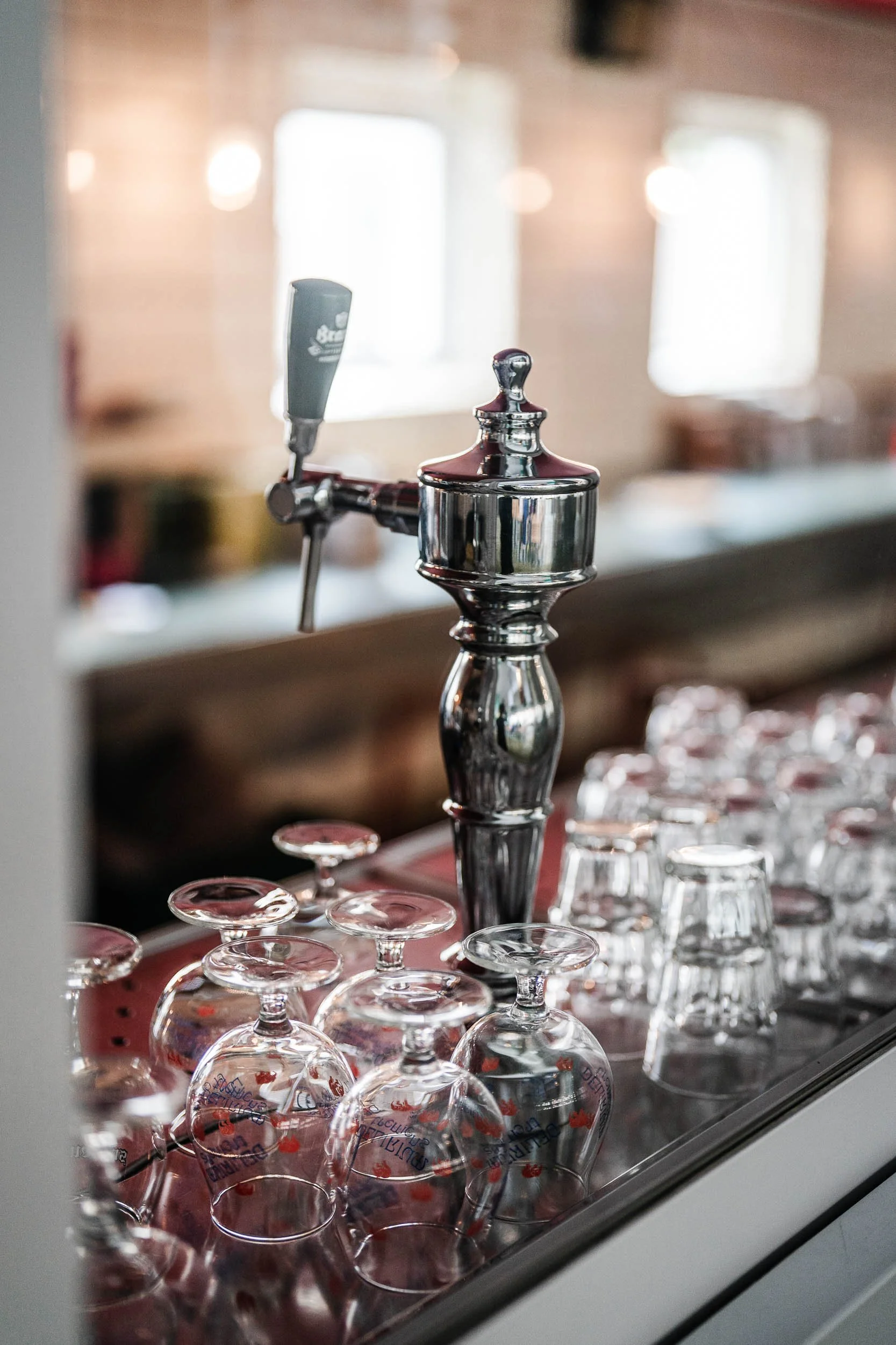 A chrome beer tap with a black handle in a bar, surrounded by upside-down glasses on a metal counter.