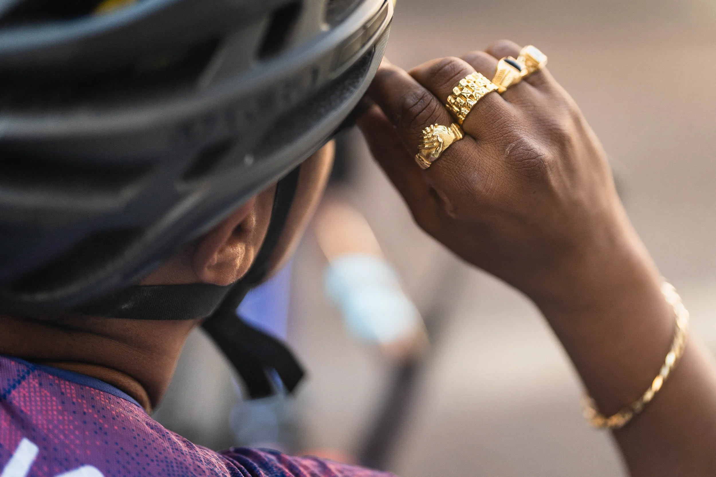 A person wearing a helmet, gold rings, and a bracelet is holding the helmet with their hand. (Patta.nl Rapha)