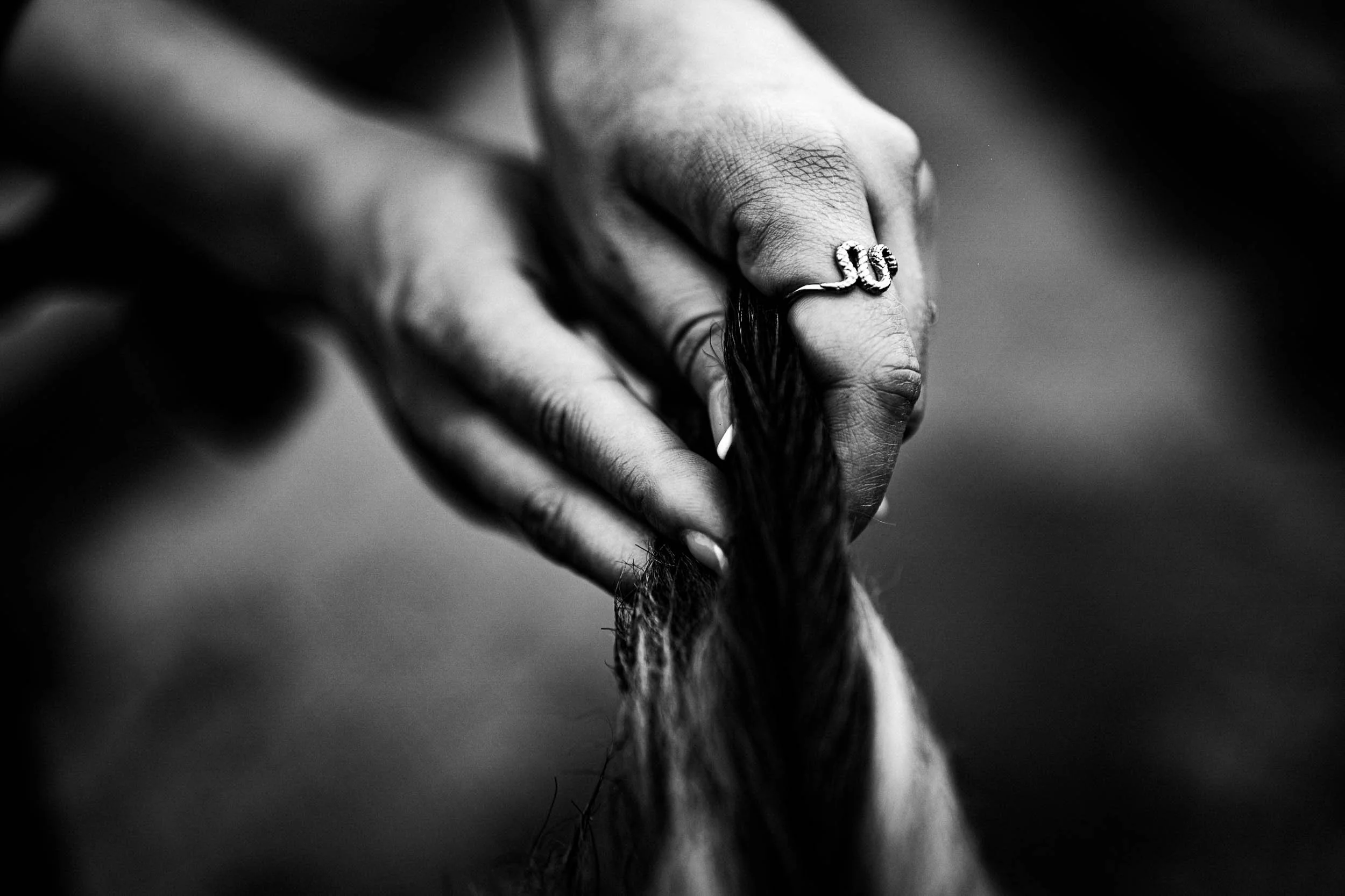 Close-up of a hand with a snake-shaped ring, holding a strand of hair or fur, in black and white.