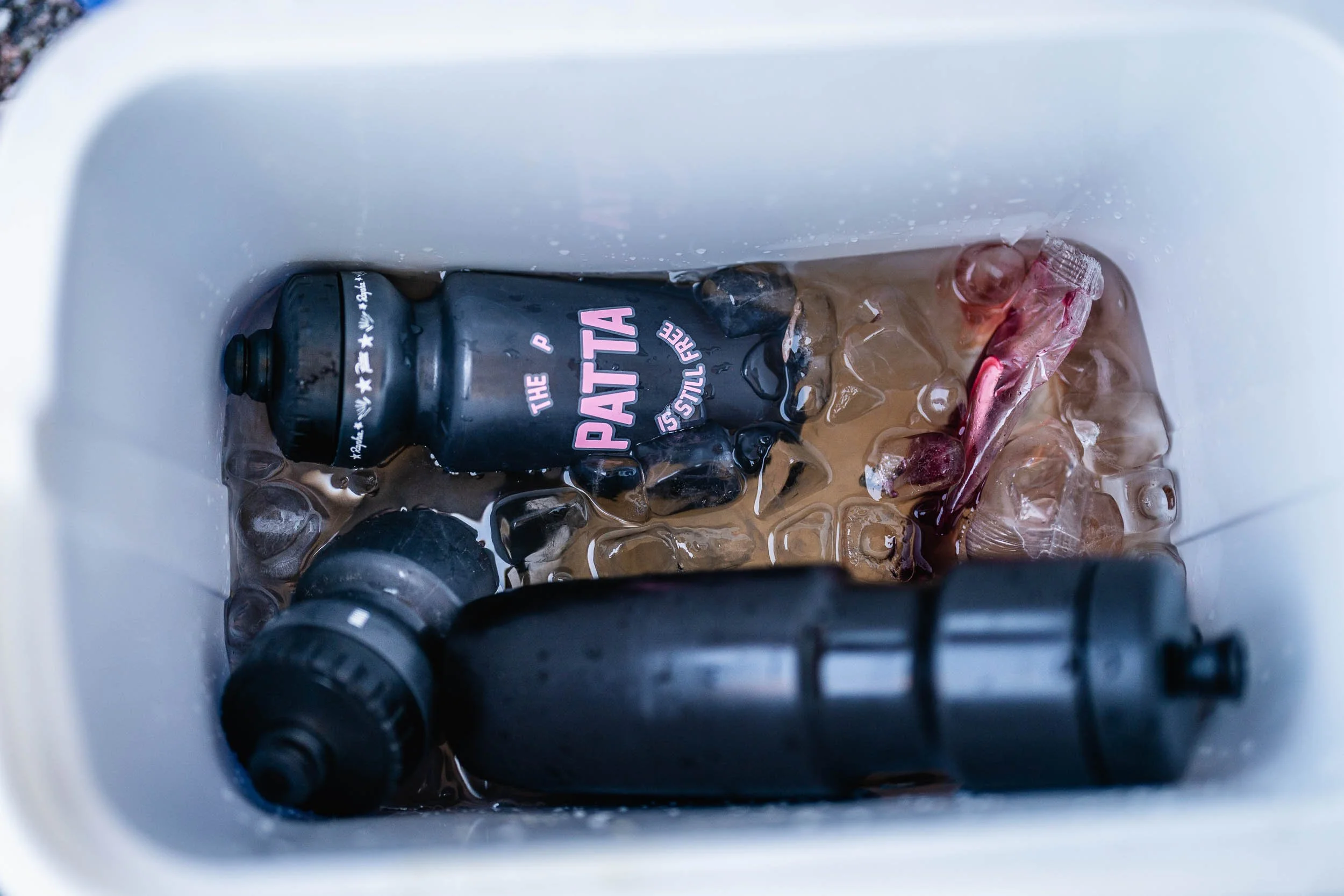 A cooler with ice, a black water bottle labeled 'The Patta is Swill Free', and objects that appear to be ice cubes and a red fish. (Patta.nl Rapha)