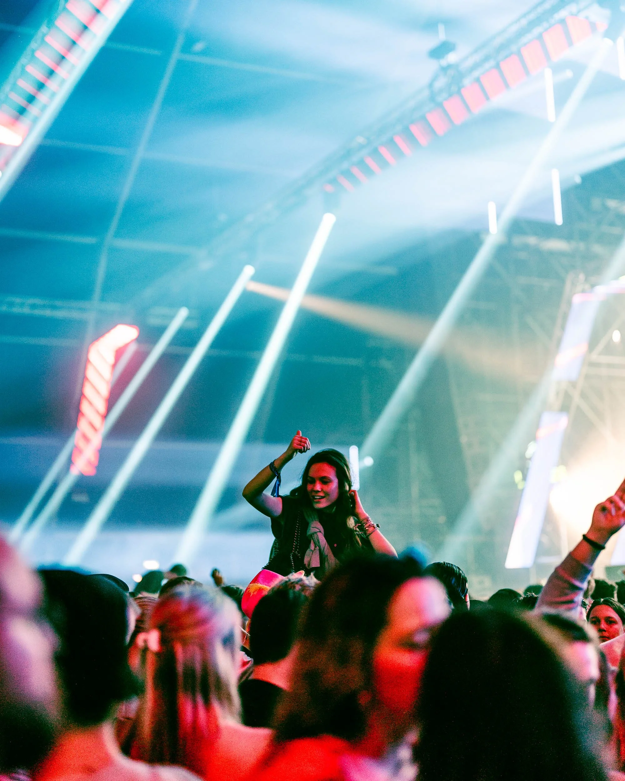 Crowd of people at a concert with stage lights and smoke effects, a woman standing on someone's shoulders dancing.   (Viktor Verhulst)