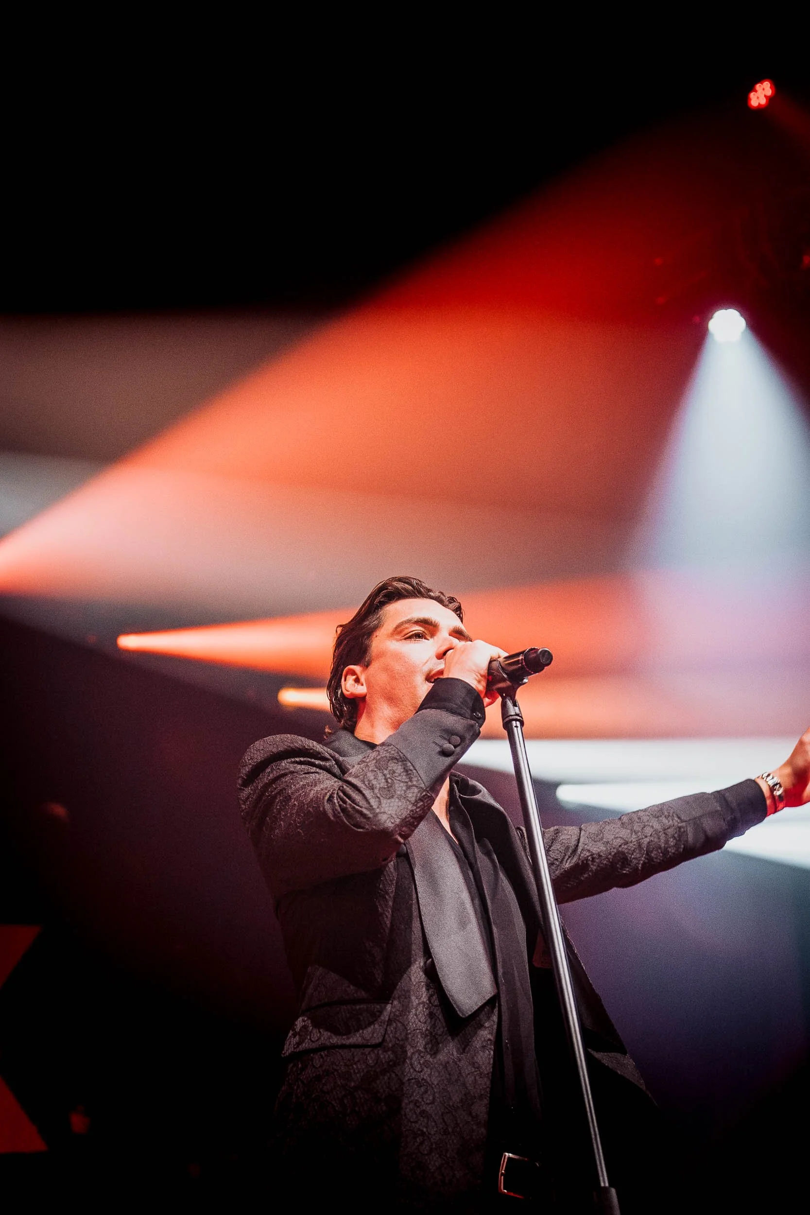 A man singing into a microphone on stage with colorful stage lighting.