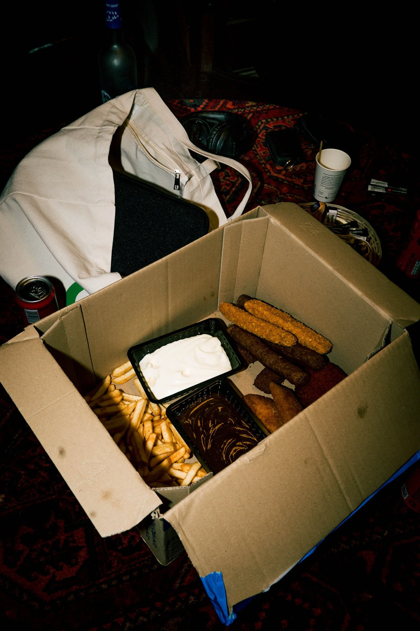 Open pizza box with French fries, chicken tenders, and dipping sauces on a table surrounded by various items like a bag, drink cups, and snacks.   (Viktor Verhulst)