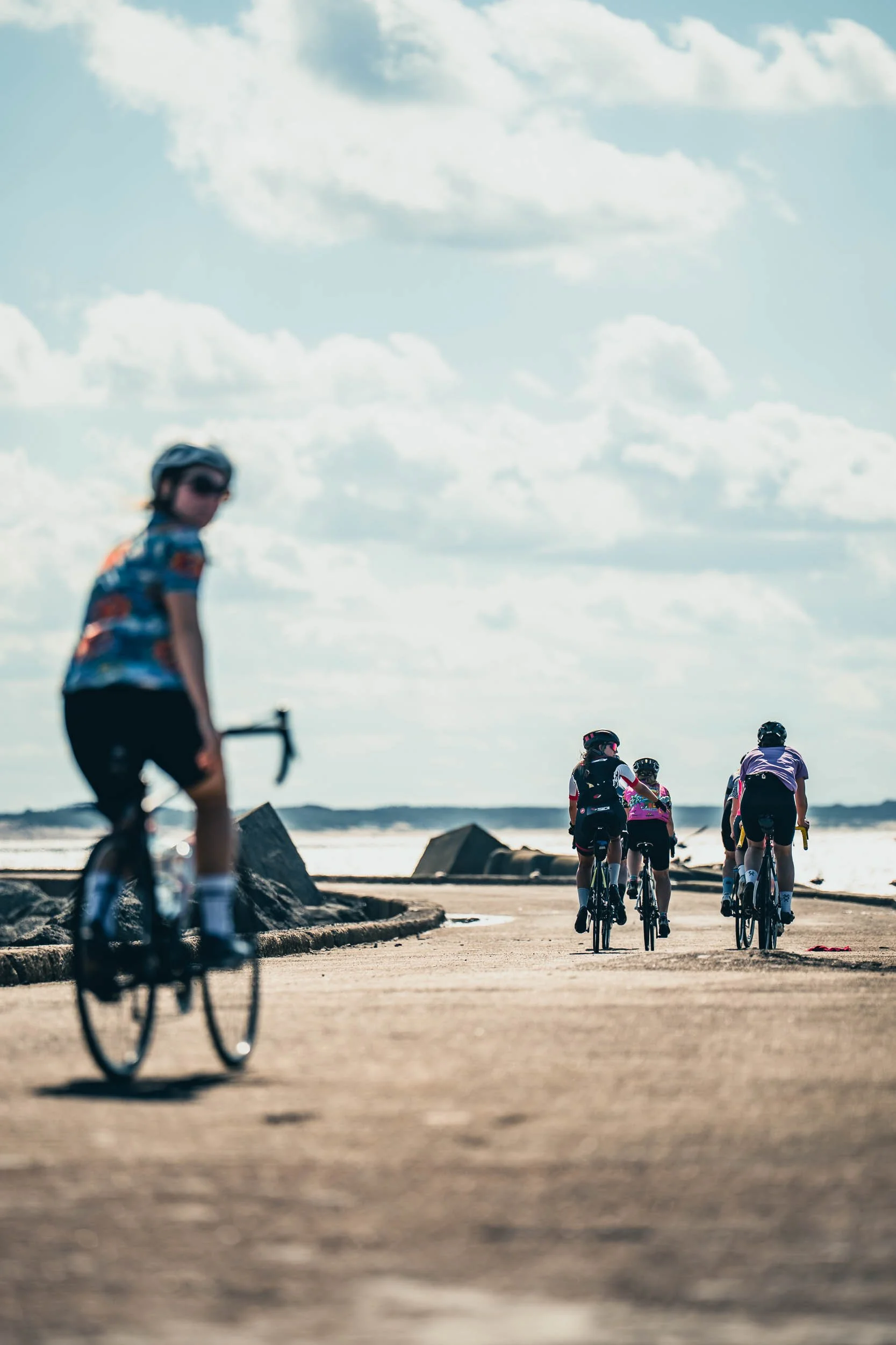 Group of children riding bicycles along a coastal path under a cloudy sky.